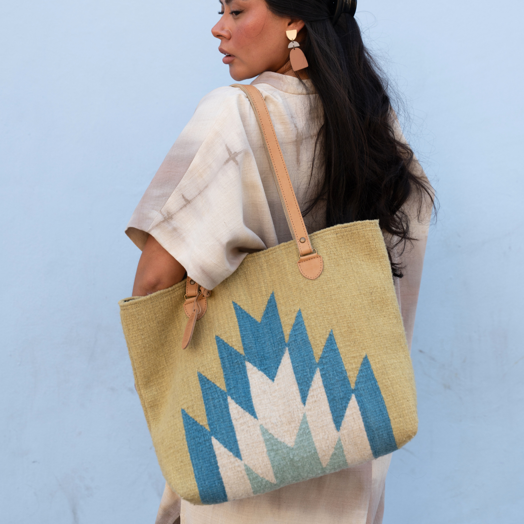 Woman carrying Zapotec handwoven tote bag with blue and green lightning design, leather straps, and interior pocket; spacious and stylish for everyday use