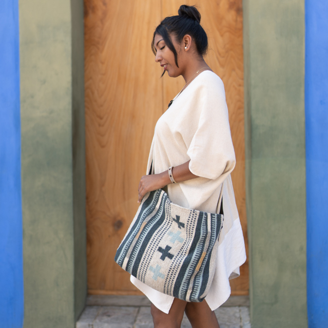 Effortlessly chic woman carrying an AMASOUK Copalita handwoven wool and leather convertible shoulder/crossbody bag with blue, cream, honey, and gray hues. A versatile accessory for any occasion.