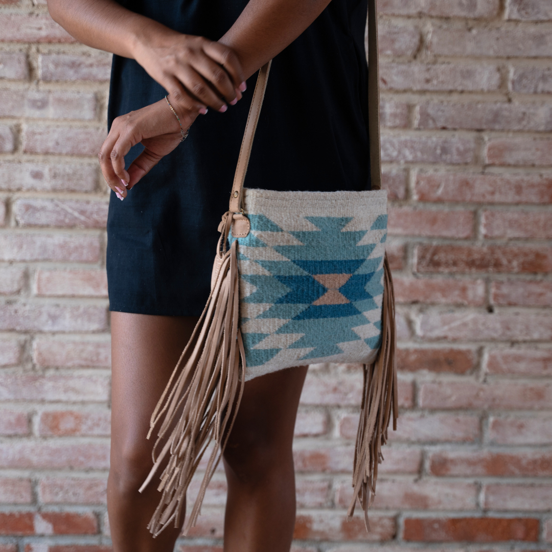 Woman carrying Handwoven fringe crossbody bag with abstract Zapotec diamond design in soft spring colors; features adjustable leather strap and two internal pockets