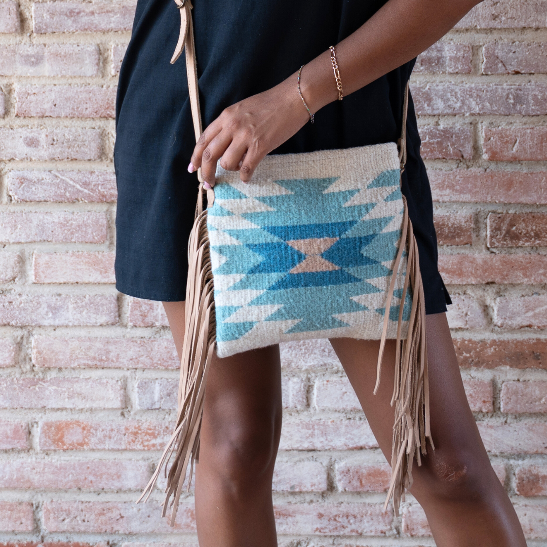 Woman carrying Handwoven fringe crossbody bag with abstract Zapotec diamond design in soft spring colors; features adjustable leather strap and two internal pockets