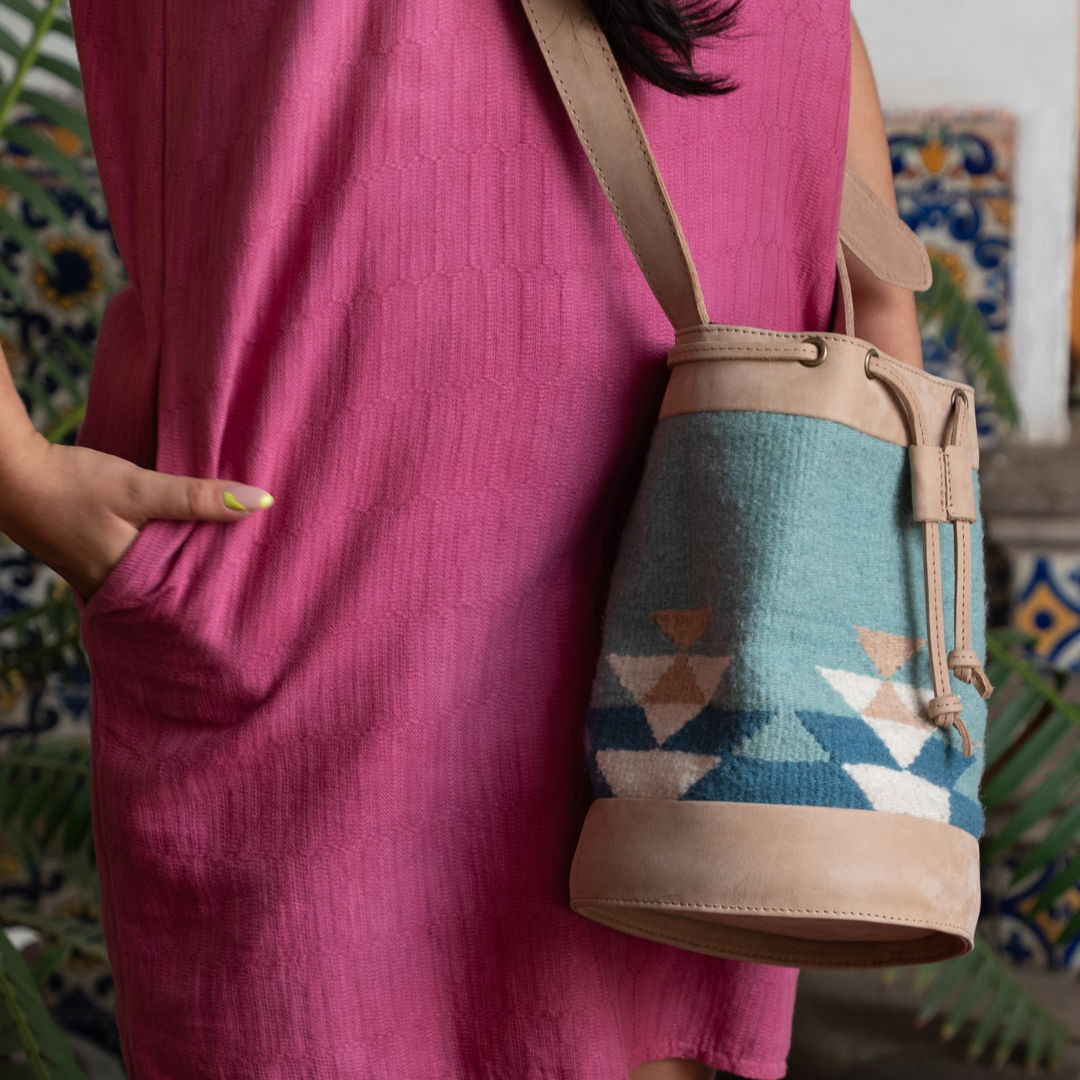 Handwoven blue wool and leather cinched bucket bag with adjustable strap, featuring a soft silhouette inspired by river currents; artisan-made and spacious.