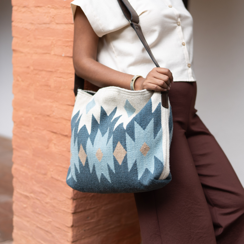 Woman carrying an AMASOUK handwoven wool Alcala Shoulder/Crossbody Bag in blue, ivory, and honey colors. Ideal for errands, work, or casual outings.
