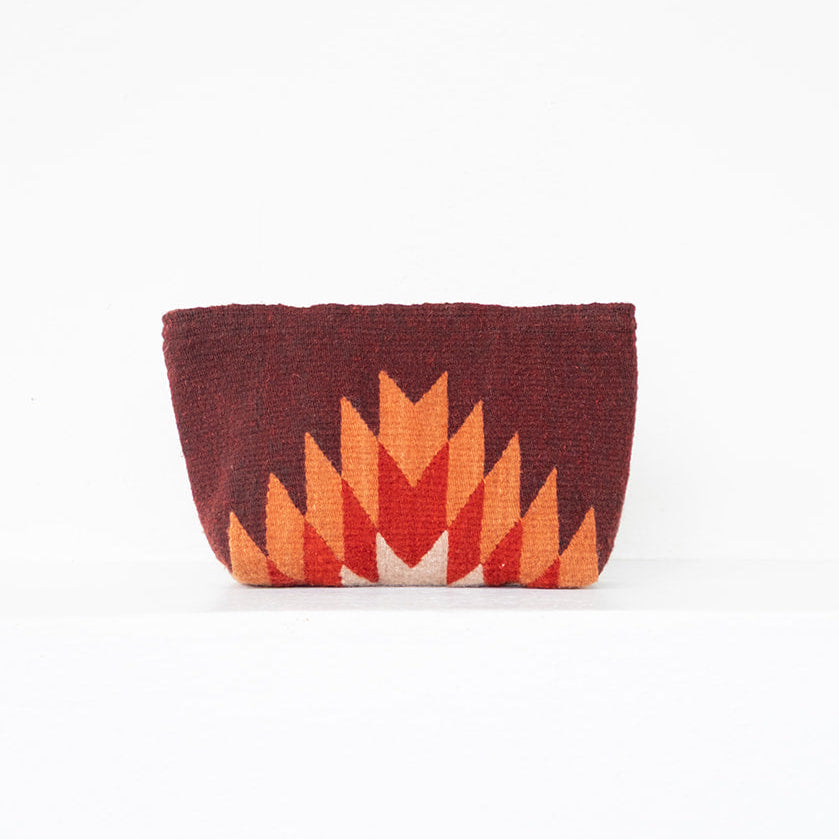 A small woven clutch bag with a Southwestern geometric pattern in dark red, orange, and cream, set against a plain white background.