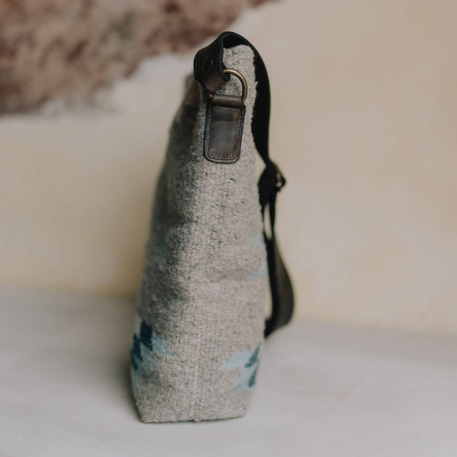 Side view AMASOUK handwoven wool Aguila Shoulder/Crossbody bag in a Zapotec pattern with blue, ivory, and honey on a gray background. Effortlessly stylish for day-to-night use.