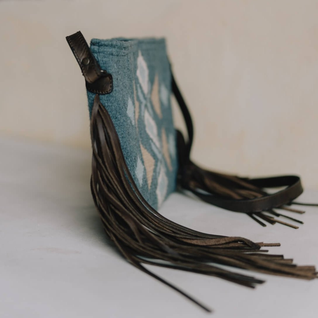 Side view of Festive AMASOUK Jalisco Fringe Crossbody featuring a dark brown leather strap, side fringe, and handwoven wool in blue, heather gray, and honey. Embellished with traditional Zapotec patterns.