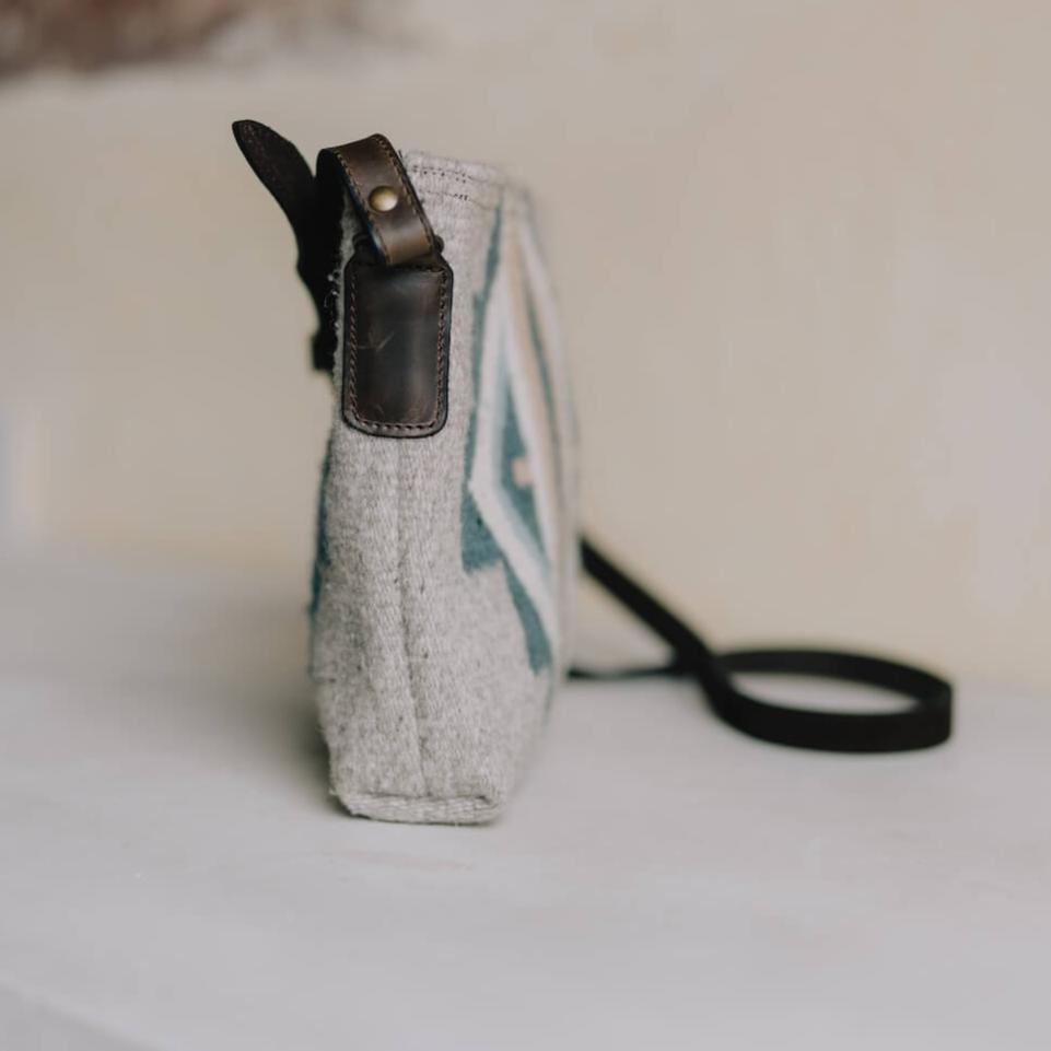 Side view of AMASOUK Sueños Crossbody bag with dark brown leather strap, handwoven wool in blue, heather gray, and ivory, and unique Zapotec patterns. Perfect for day-to-day style.
