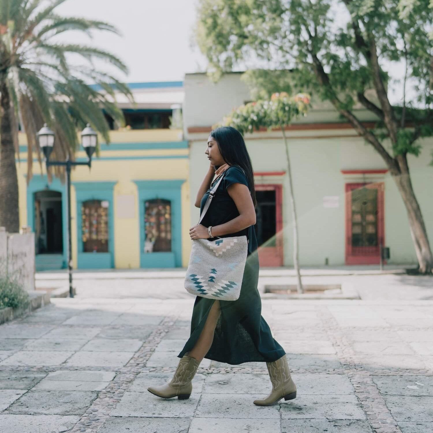 Effortlessly chic woman carrying an AMASOUK handwoven wool Aguila Shoulder/Crossbody bag with a Zapotec design in blue, ivory, and honey on a gray background. A versatile accessory for any occasion.