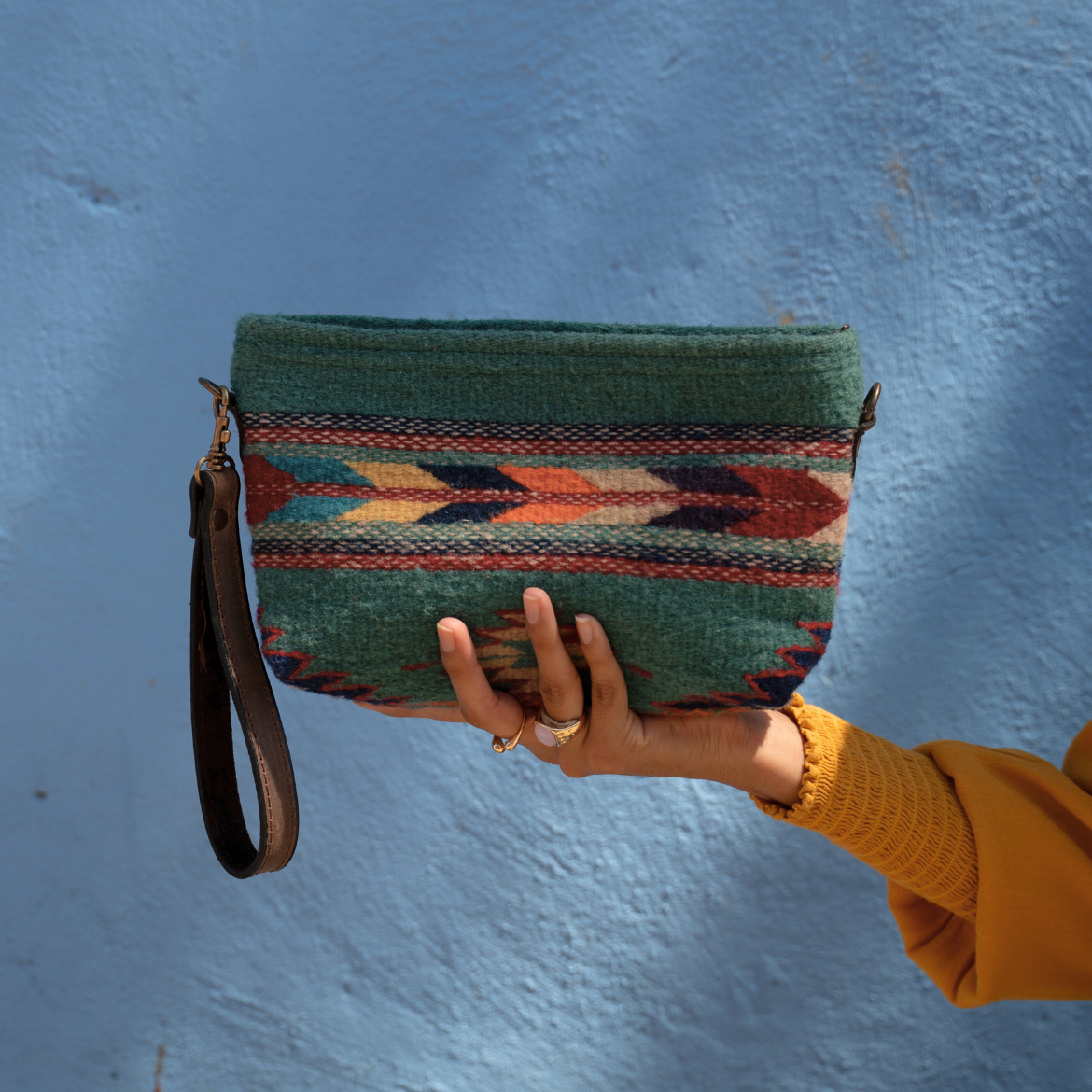 Person holding a green patterned clutch against a blue wall