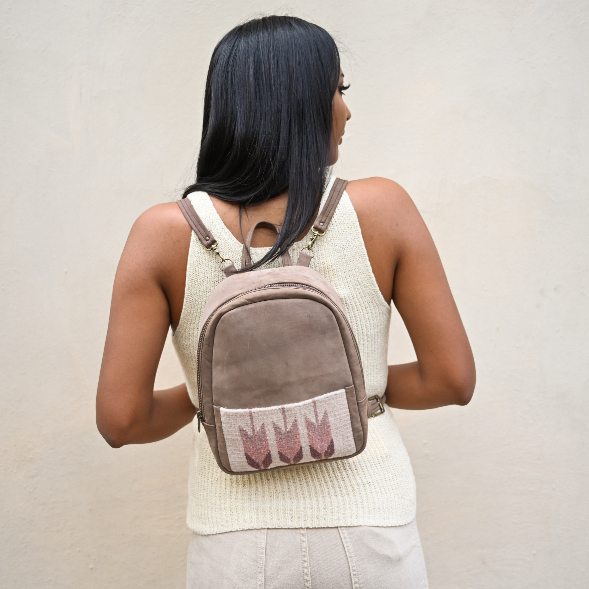Woman wearing the AMASOUK Raiz Mini Backpack with brown leather and handwoven burgundy and cream wool, featuring a Zapotec pattern. A perfect companion for work or outings.