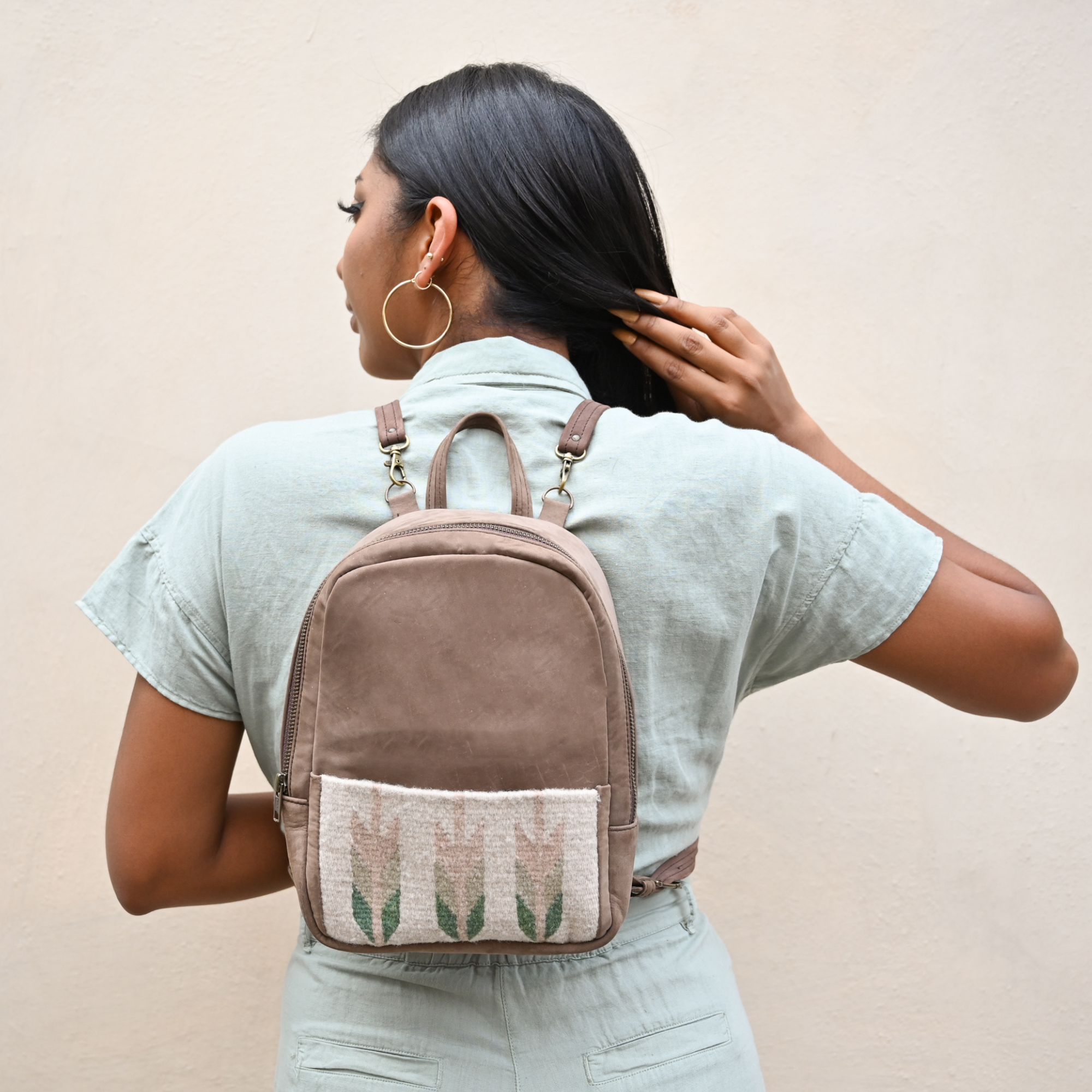 Fashionable woman wearing the AMASOUK Arbol Mini Backpack made from brown leather and light green and cream wool. Perfect for day trips and casual outings.