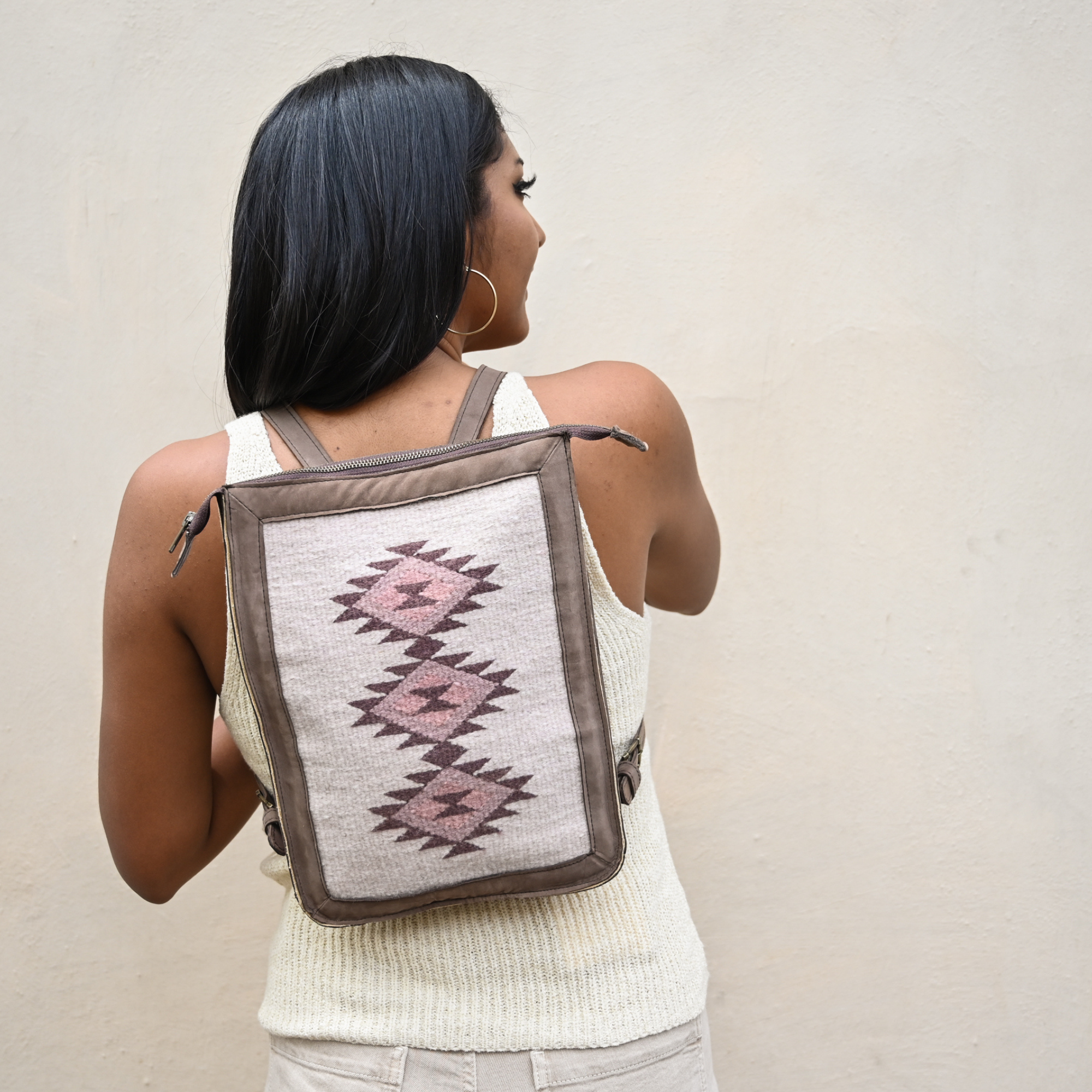 Woman carrying an AMASOUK Mora Slim Backpack, featuring dark brown leather and handwoven wool in cream and rosy tones. Stylish and practical for everyday use.
