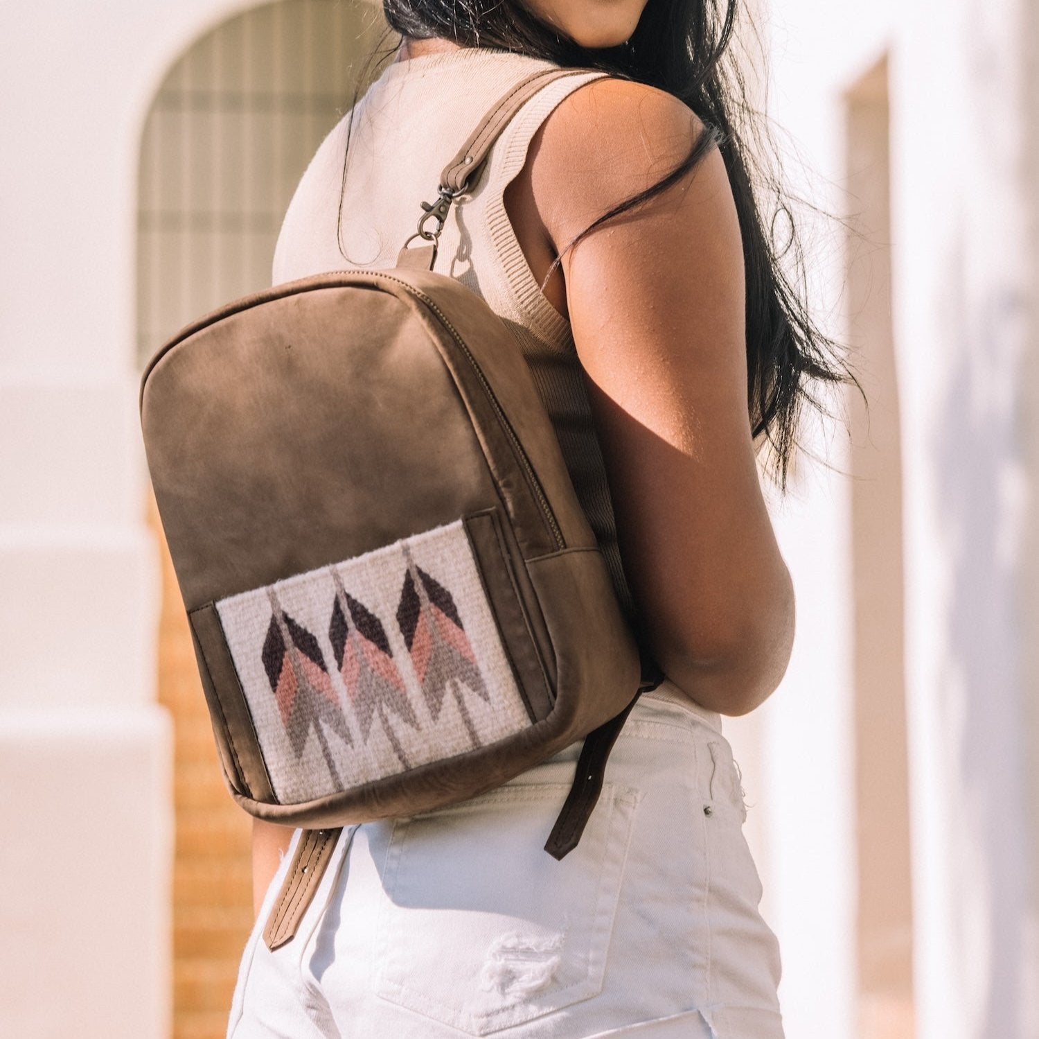 Woman wearing the AMASOUK Raiz Mini Backpack with brown leather and handwoven burgundy and cream wool, featuring a Zapotec pattern. A perfect companion for work or outings.