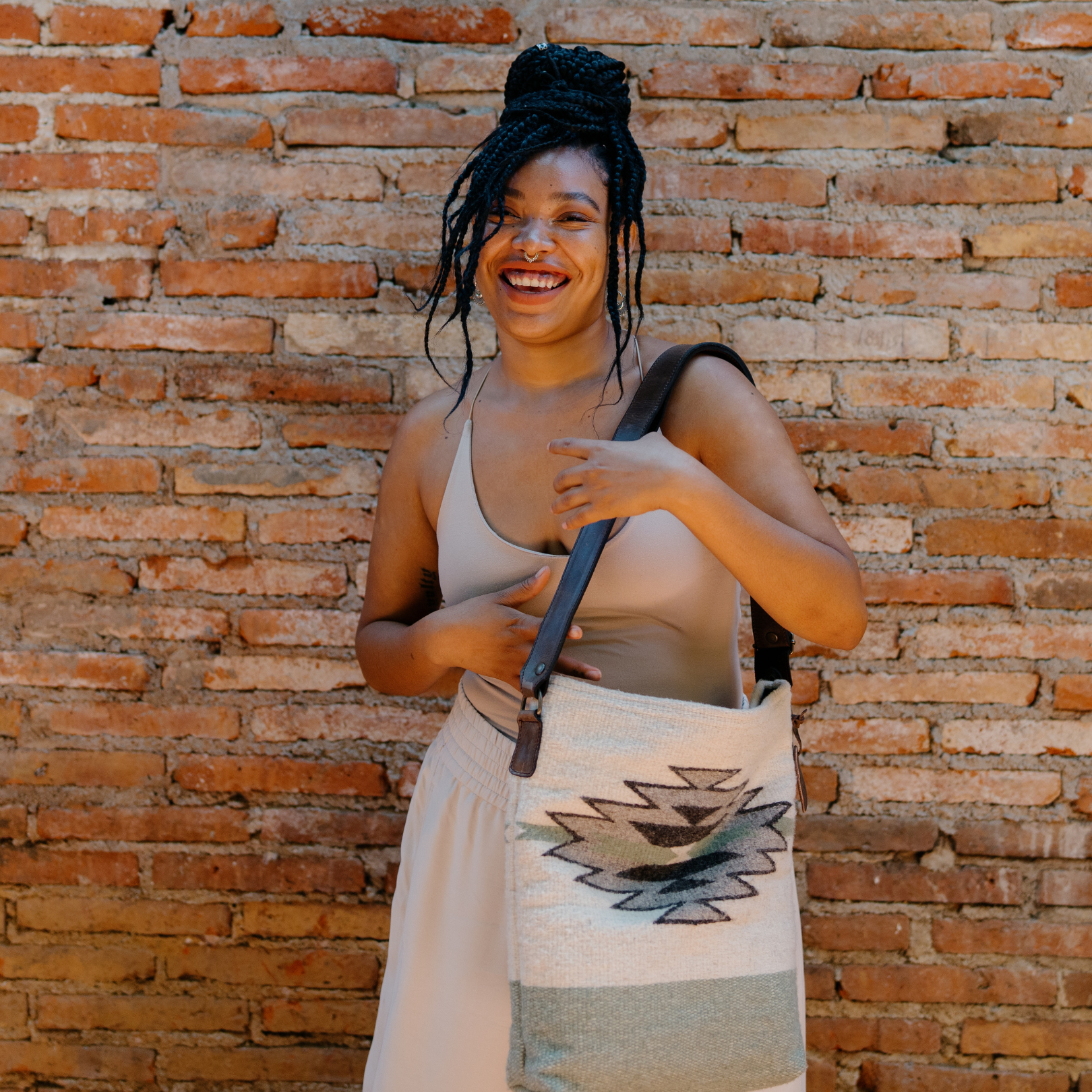 Fashionable woman with an AMASOUK handwoven wool and leather Sendero convertible shoulder/crossbody bag in a color scheme of pale green, off-white, and muted gray. Ideal for day-to-night versatility.