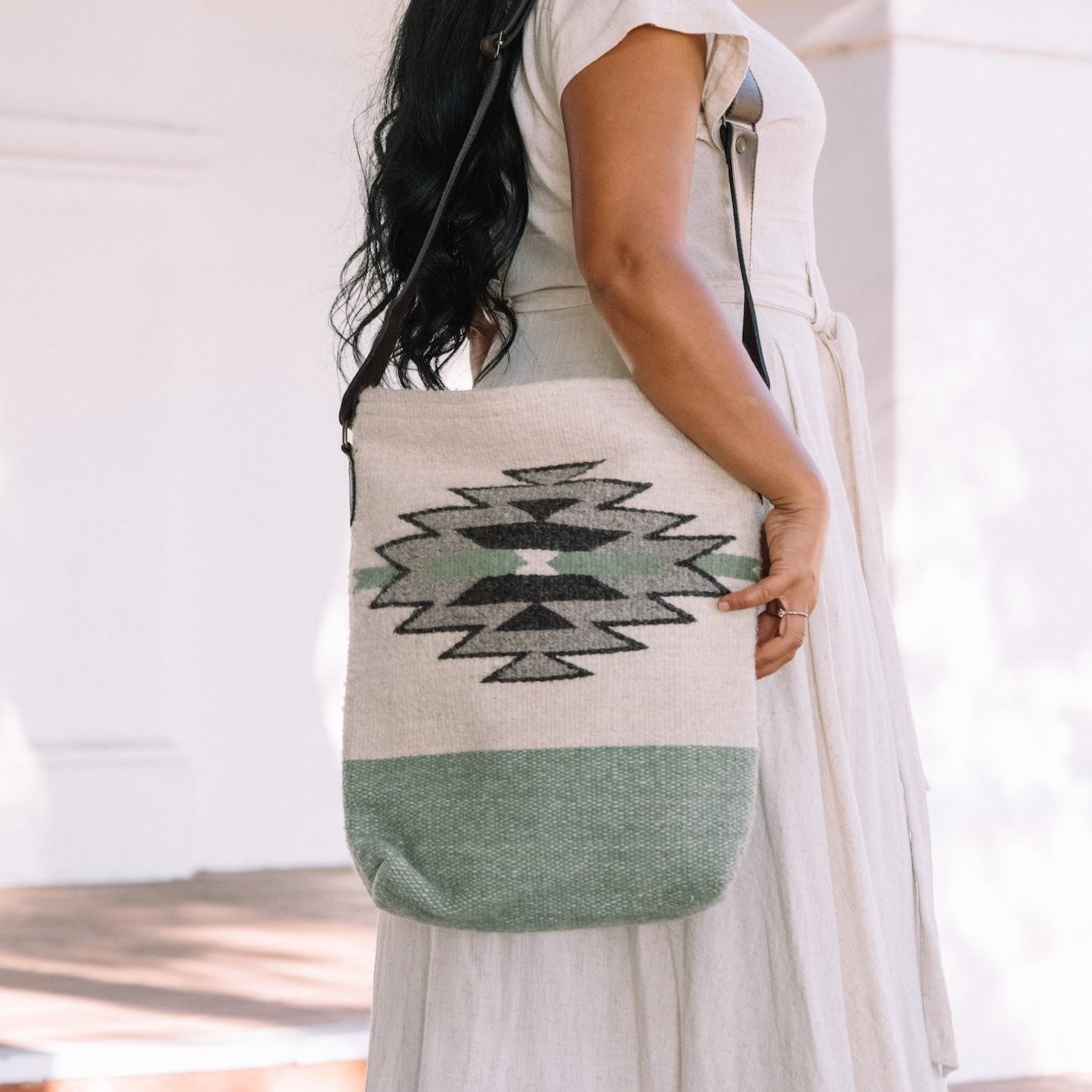 Woman holding an AMASOUK handwoven wool and leather Sendero convertible shoulder/crossbody bag with a sophisticated mix of pale green, creamy white, and light gray. Ideal for carrying essentials throughout the day.
