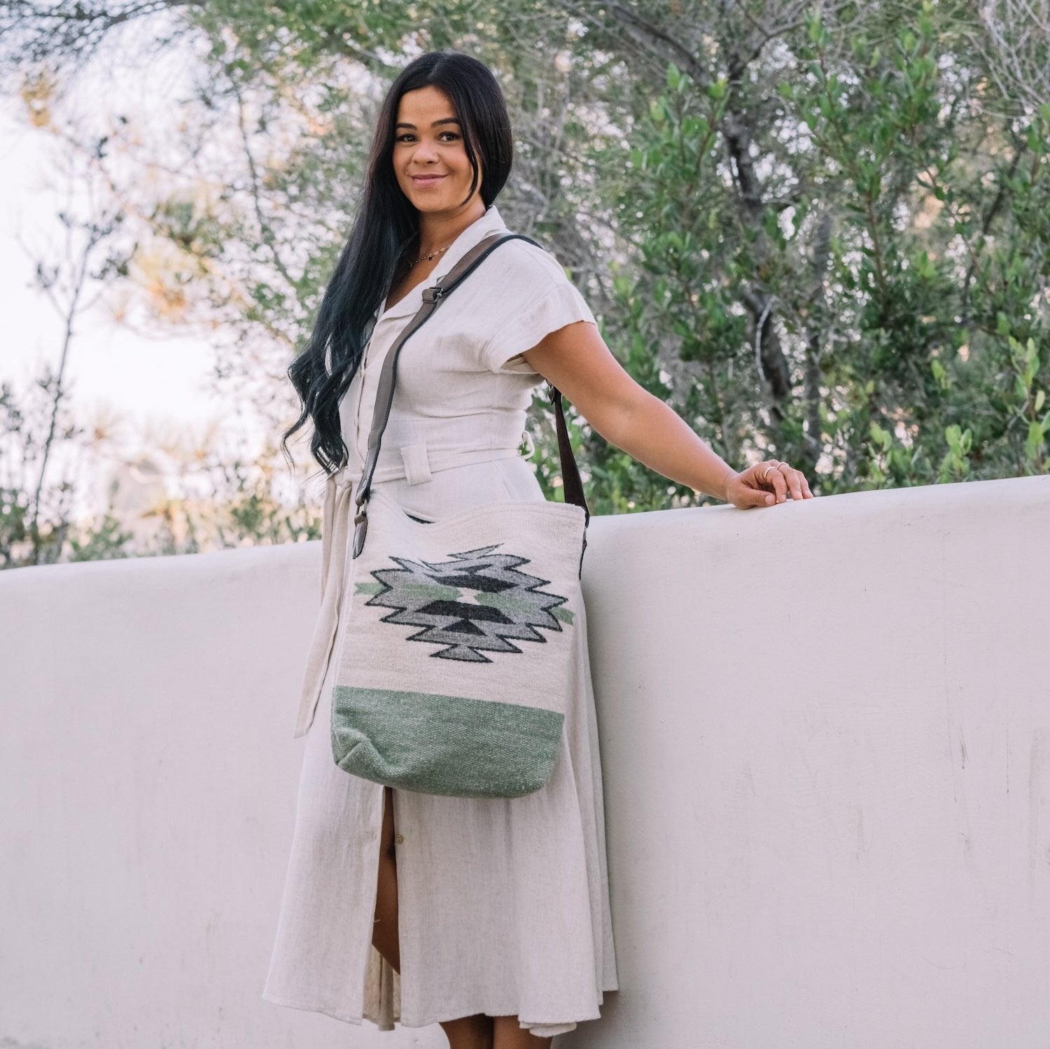 Effortlessly chic woman carrying an AMASOUK handwoven wool and leather Sendero convertible shoulder/crossbody bag in a blend of gentle green, ivory, and soft gray. A versatile accessory for any occasion.