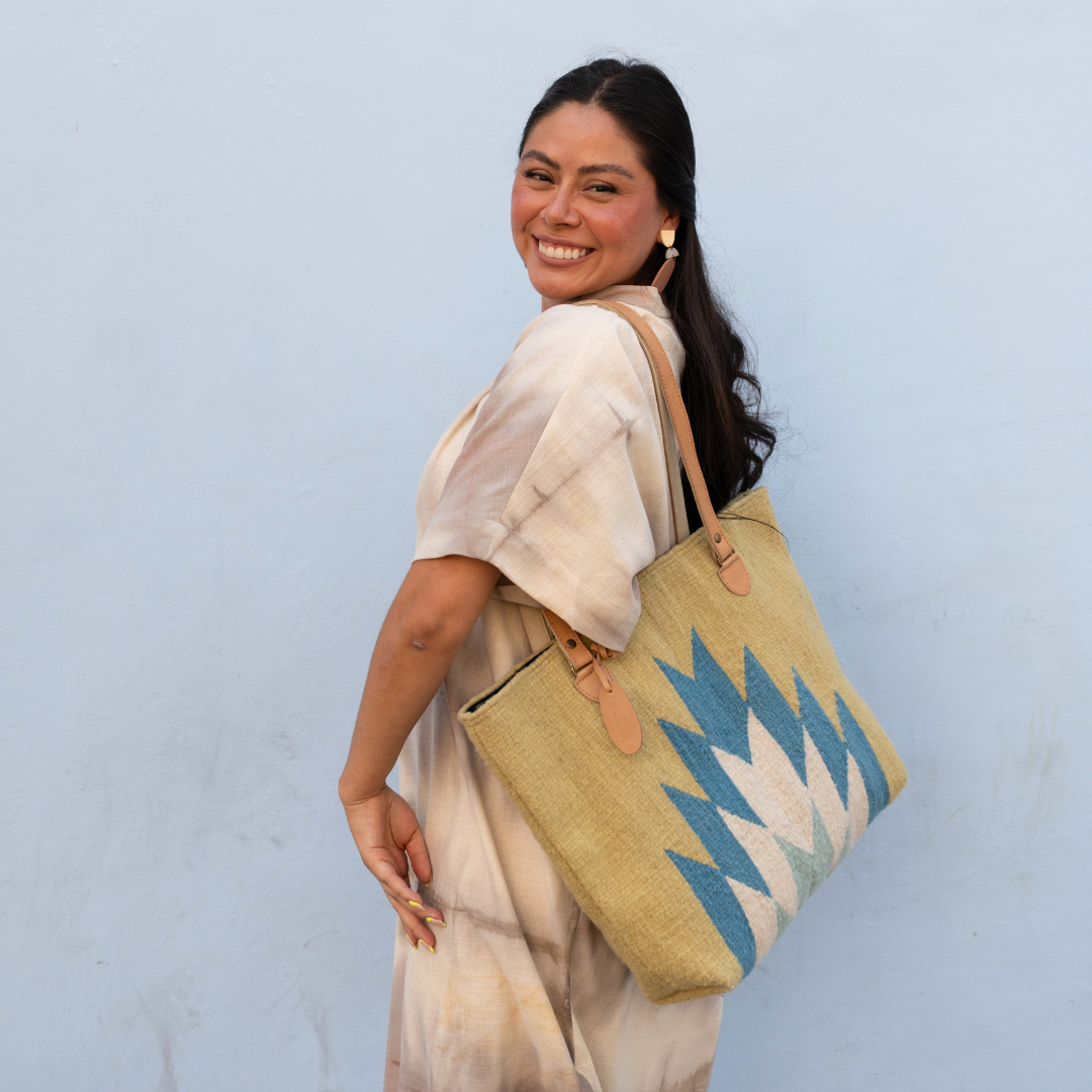 Woman carrying Zapotec handwoven tote bag with blue and green lightning design, leather straps, and interior pocket; spacious and stylish for everyday use