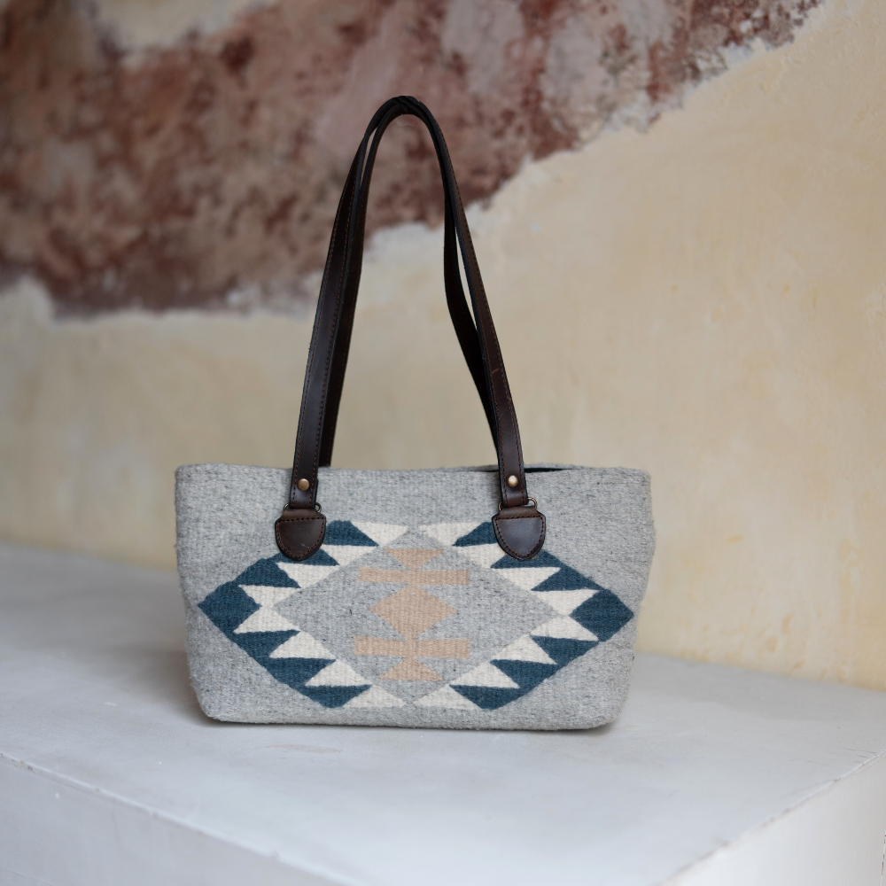 AMASOUK handwoven wool purse with Dainzu name, featuring a Zapotec pattern in soft sky, creamy off-white, and warm golden tones. A stylish and versatile accessory for any occasion.