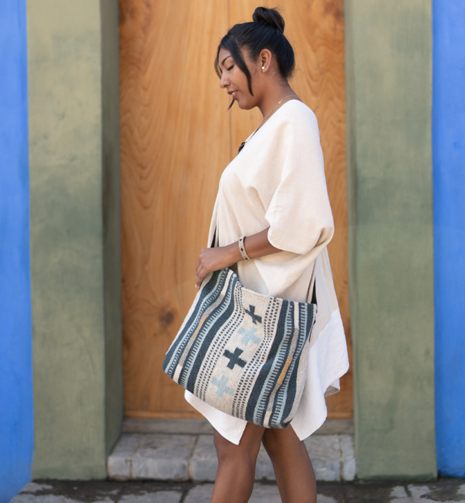 Effortlessly chic woman carrying an AMASOUK Copalita handwoven wool and leather convertible shoulder/crossbody bag with blue, cream, honey, and gray hues. A versatile accessory for any occasion.