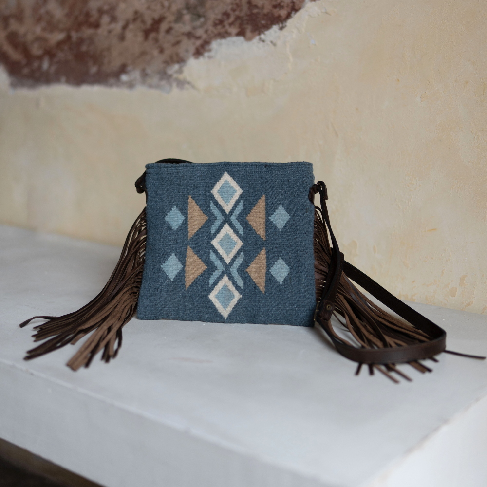 AMASOUK Jalisco Fringe Crossbody with dark brown leather strap, featuring fringe on the sides and handwoven wool in blue, heather gray, and honey. Festive design with traditional Zapotec patterns.