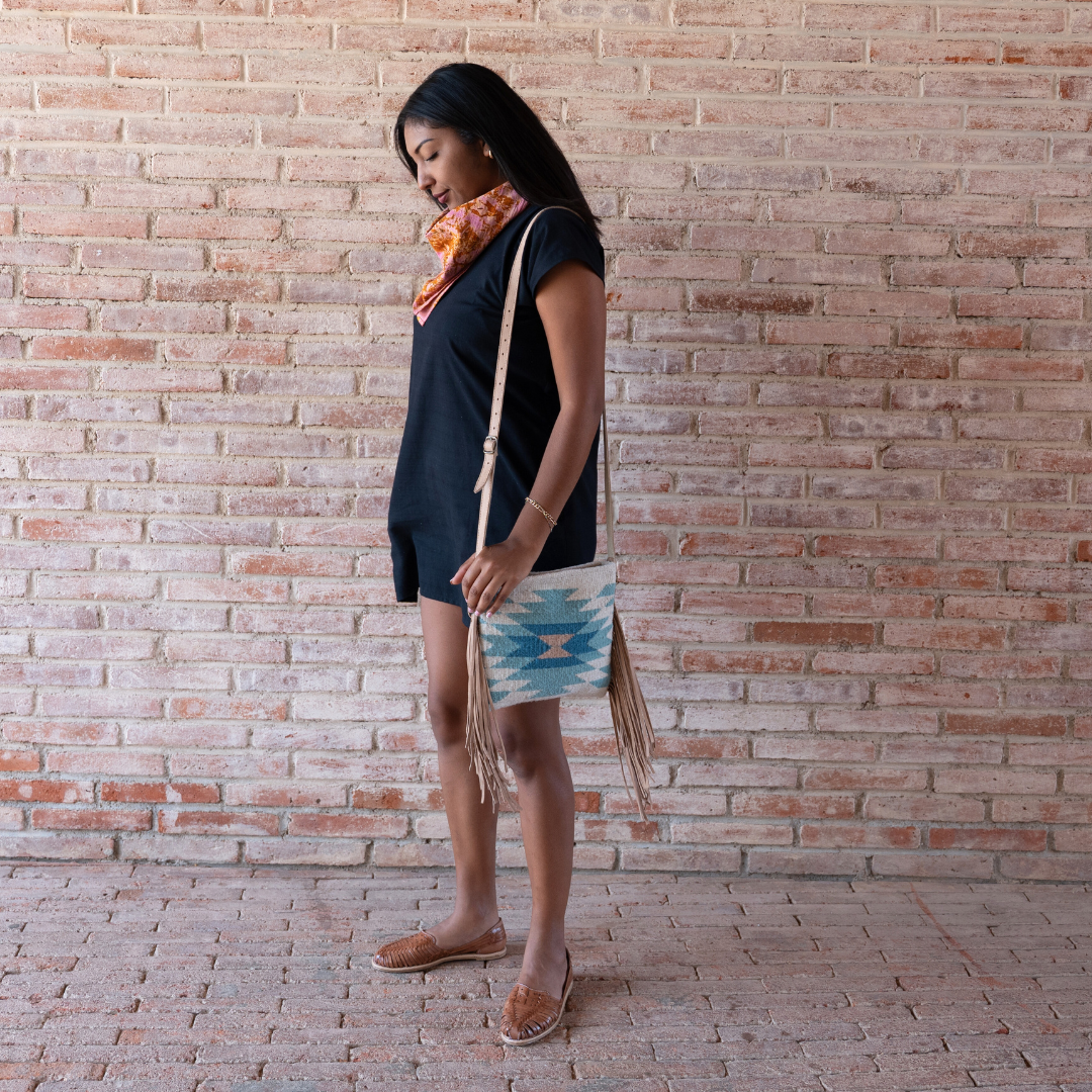 Woman carrying Handwoven fringe crossbody bag with abstract Zapotec diamond design in soft spring colors; features adjustable leather strap and two internal pockets