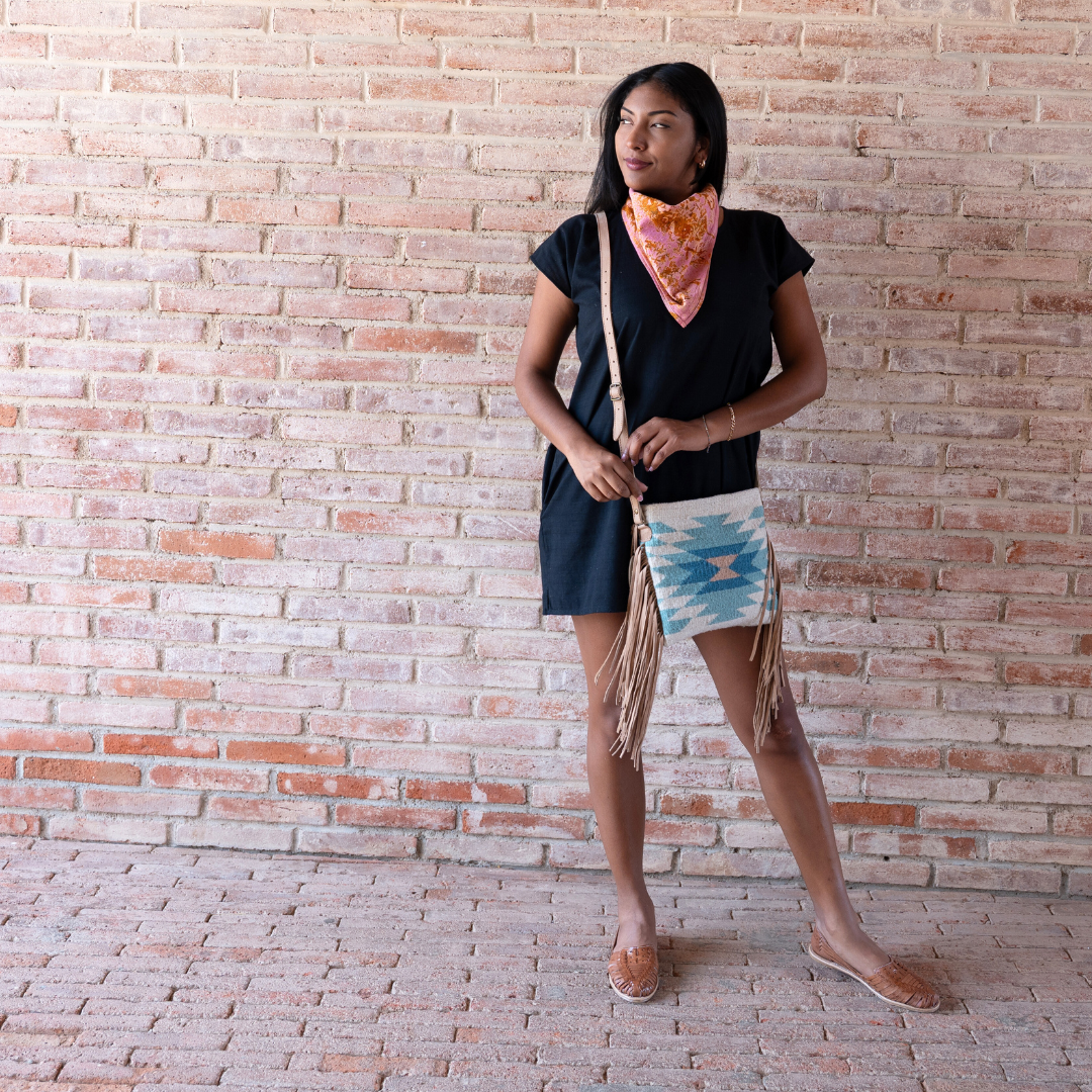 Woman carrying Handwoven fringe crossbody bag with abstract Zapotec diamond design in soft spring colors; features adjustable leather strap and two internal pockets