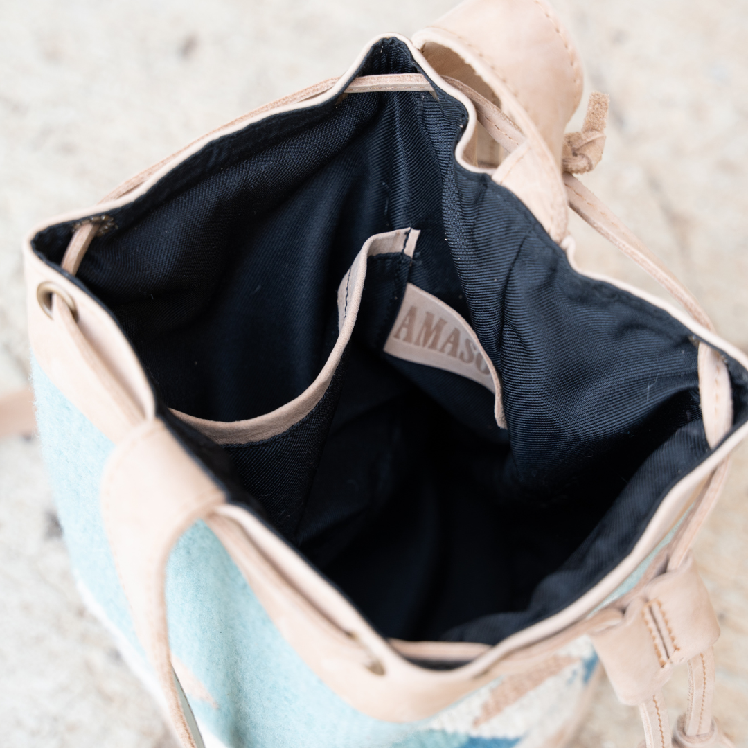 Interior view of handwoven blue wool and leather cinched bucket bag with adjustable strap, featuring a soft silhouette inspired by river currents; artisan-made and spacious.