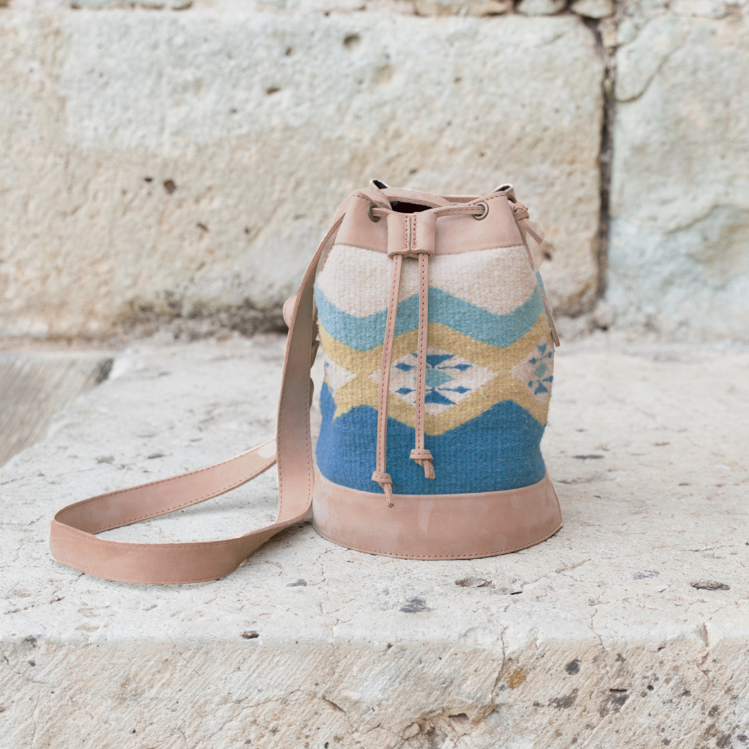 Colibrí Cinched Bucket Bag in handwoven wool and leather with green and blue Zapotec diamond and butterfly pattern, featuring an adjustable strap and cinched silhouette.