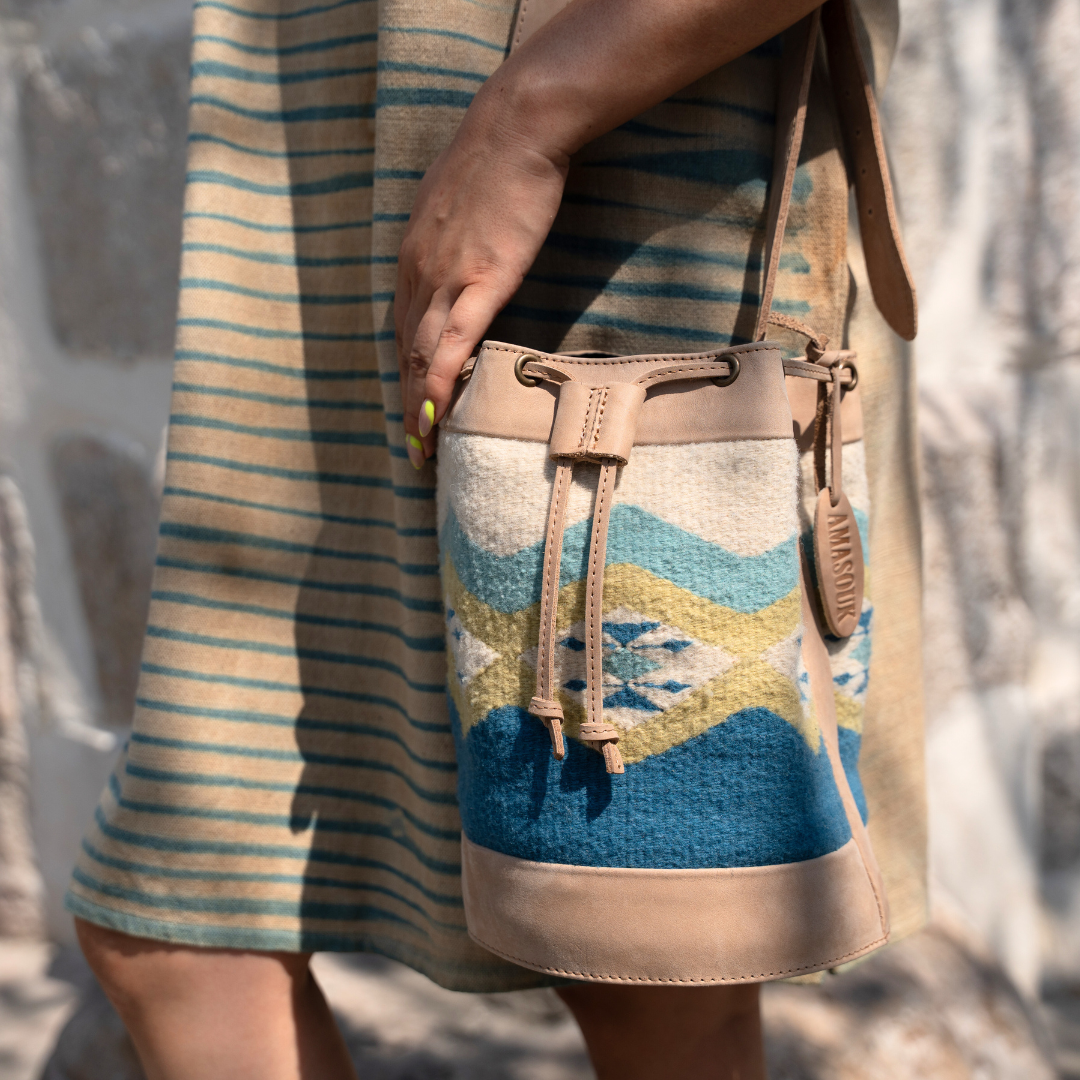 Woman carrying Colibrí Cinched Bucket Bag in handwoven wool and leather with green and blue Zapotec diamond and butterfly pattern, featuring an adjustable strap and cinched silhouette.