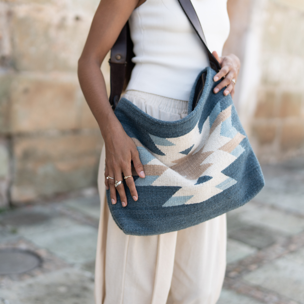 Woman carrying an AMASOUK handwoven wool Solyagaua convertible shoulder/crossbody bag in deep ocean blue, soft ivory, and warm honey tones. A perfect combination of style and functionality for any outing.