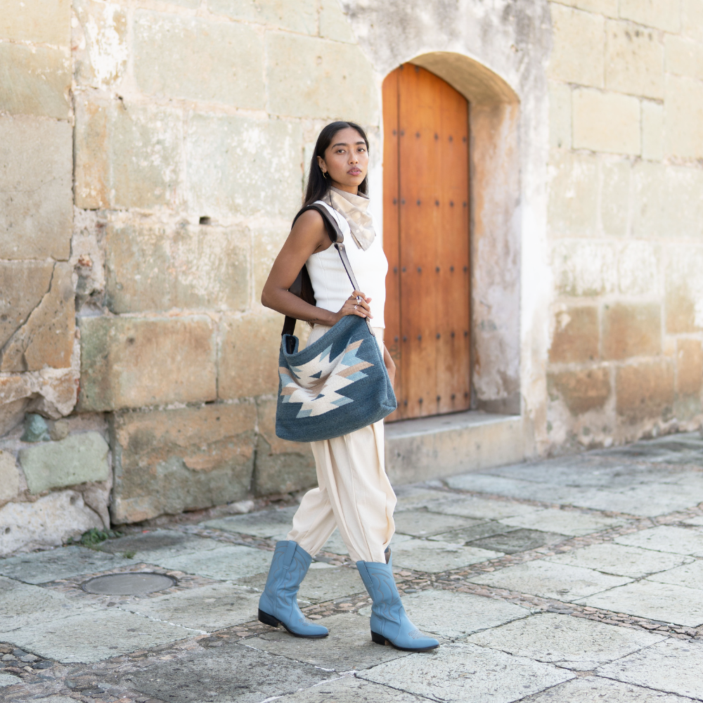 Fashionable woman with an AMASOUK handwoven wool Solyagaua convertible shoulder/crossbody bag, featuring an elegant Zapotec pattern in rich sea-blue, creamy ivory, and golden honey hues. Ideal for versatile day-to-night use.