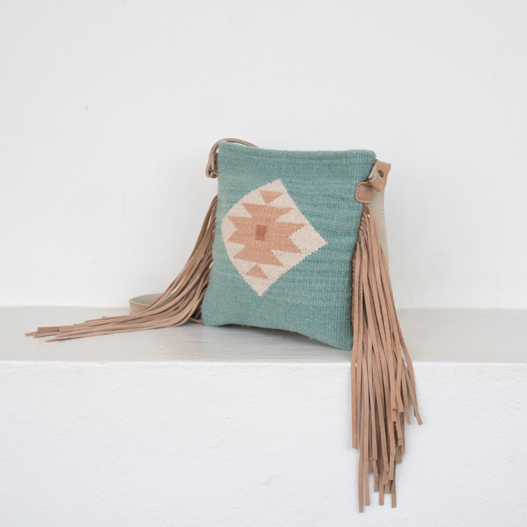 handwoven fringe crossbody bag with abstract Zapotec butterfly design in soft blue tones; features flowing fringe, adjustable leather strap, and two internal pockets
