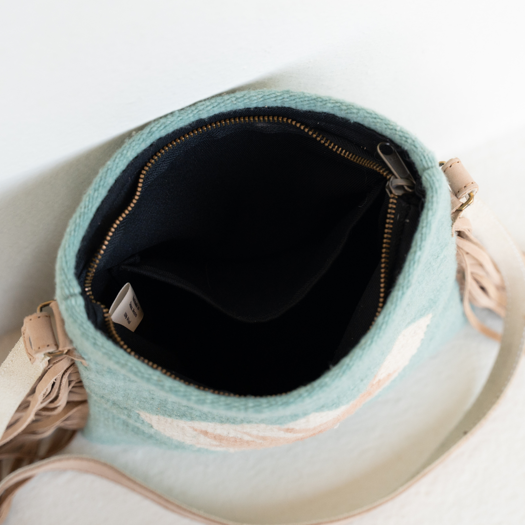 Interior view of handwoven fringe crossbody bag with abstract Zapotec butterfly design in soft blue tones; features flowing fringe, adjustable leather strap, and two internal pockets