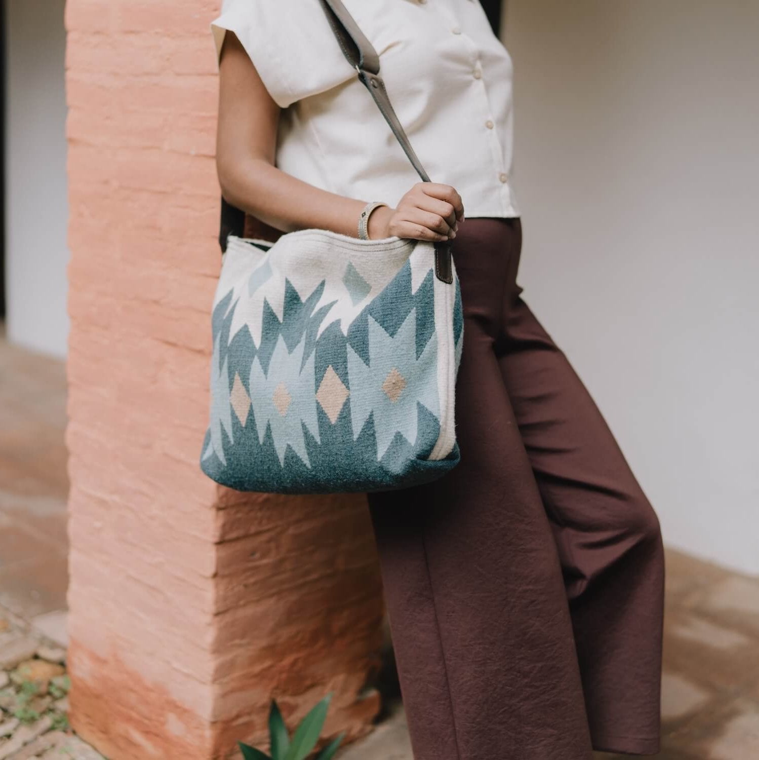 Woman carrying an AMASOUK handwoven wool Alcala Shoulder/Crossbody Bag in blue, ivory, and honey colors. Ideal for errands, work, or casual outings.