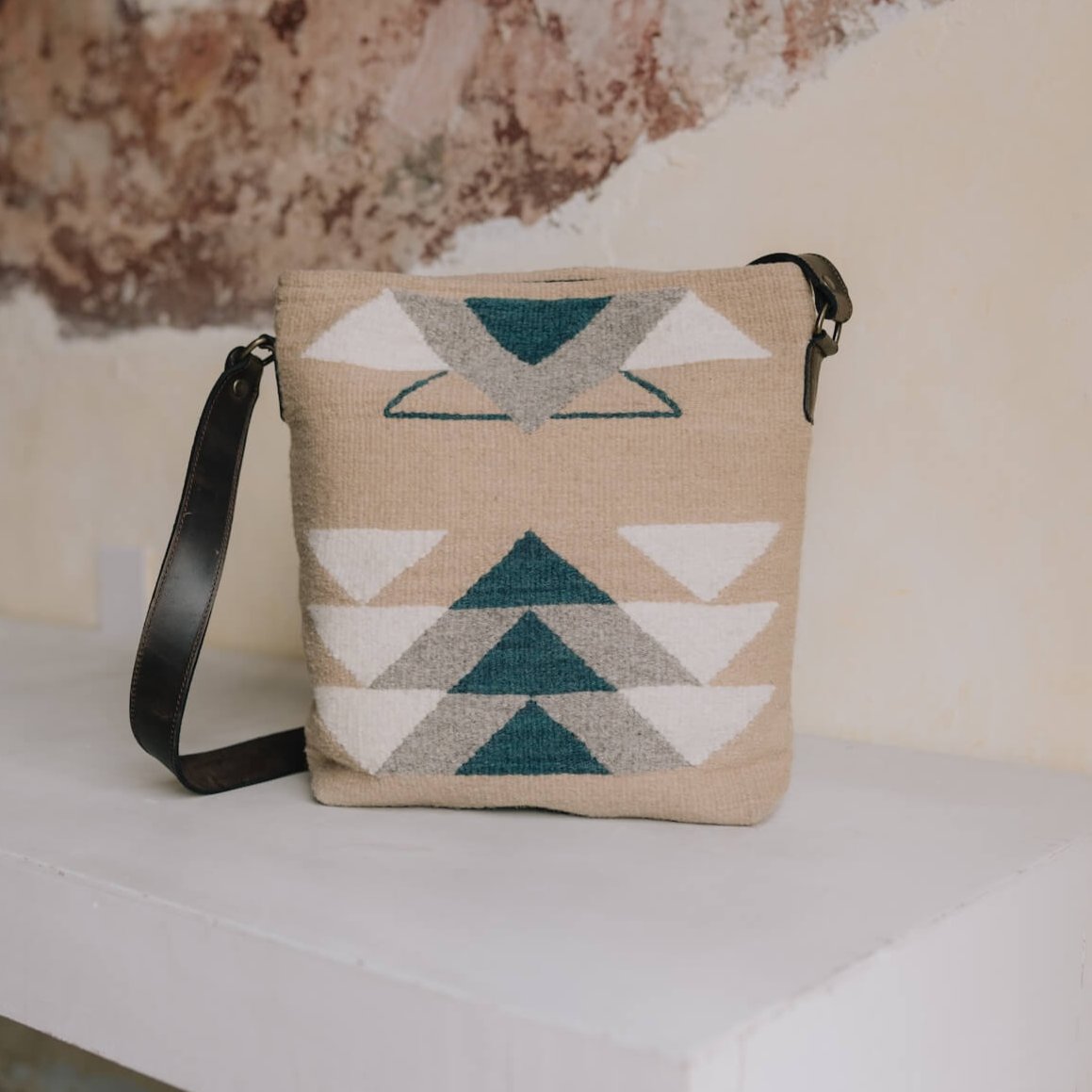 AMASOUK handwoven wool and leather Pueblo convertible shoulder/crossbody bag, featuring a blend of deep blue, soft gray, and creamy white on a neutral beige backdrop. Stylish and versatile for daily and evening use.