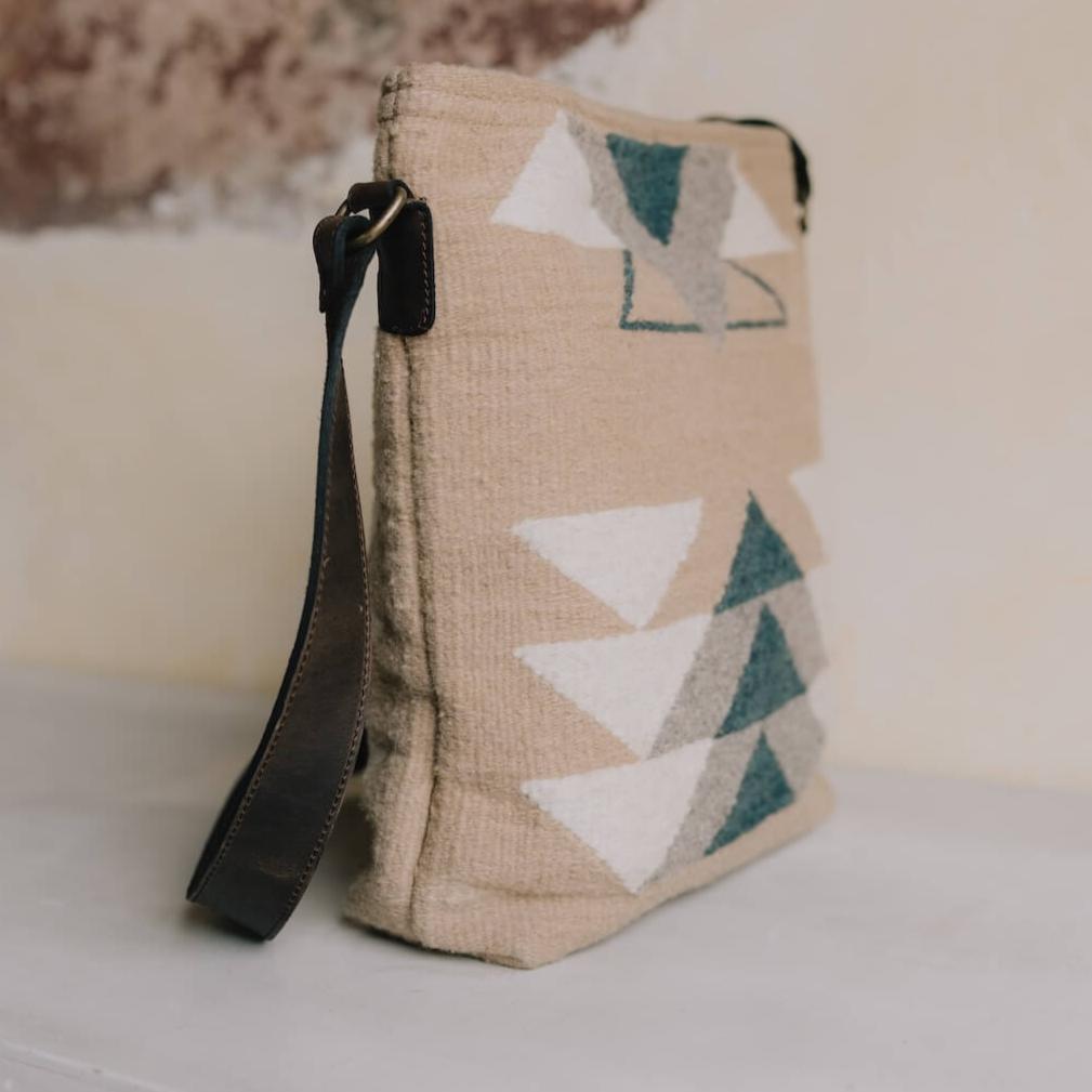 Elegant AMASOUK handwoven wool and leather Pueblo convertible shoulder/crossbody bag, showcasing a mix of navy, slate, and ivory tones on a sand-colored base. The ideal accessory for day-to-night outings.