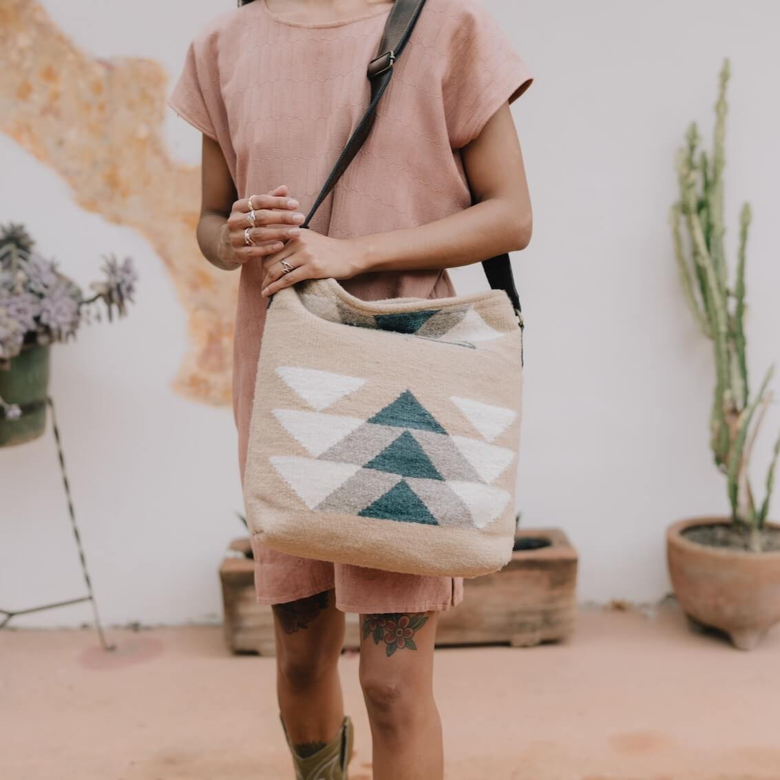 Fashionable woman with an AMASOUK handwoven wool and leather Pueblo convertible shoulder/crossbody bag in navy, slate gray, and ivory, set on a sand-colored backdrop. Ideal for day-to-night versatility.