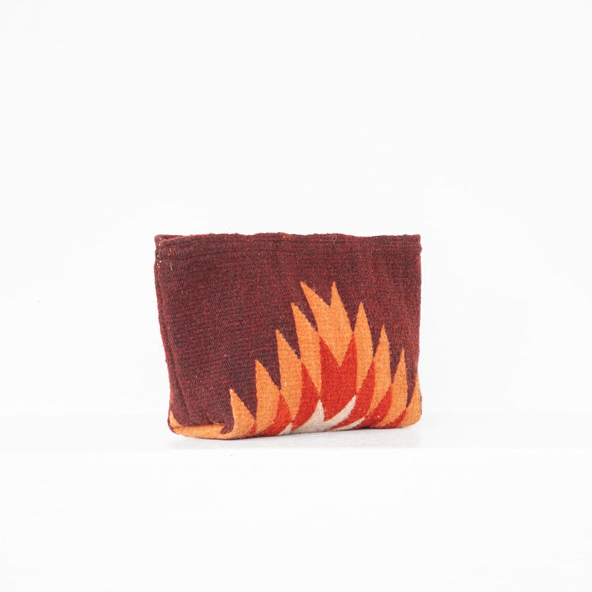 A small fabric pouch or clutch with a dark reddish-brown background and a geometric flame-like pattern in orange, yellow, and white along the lower front, photographed against a plain white background.
