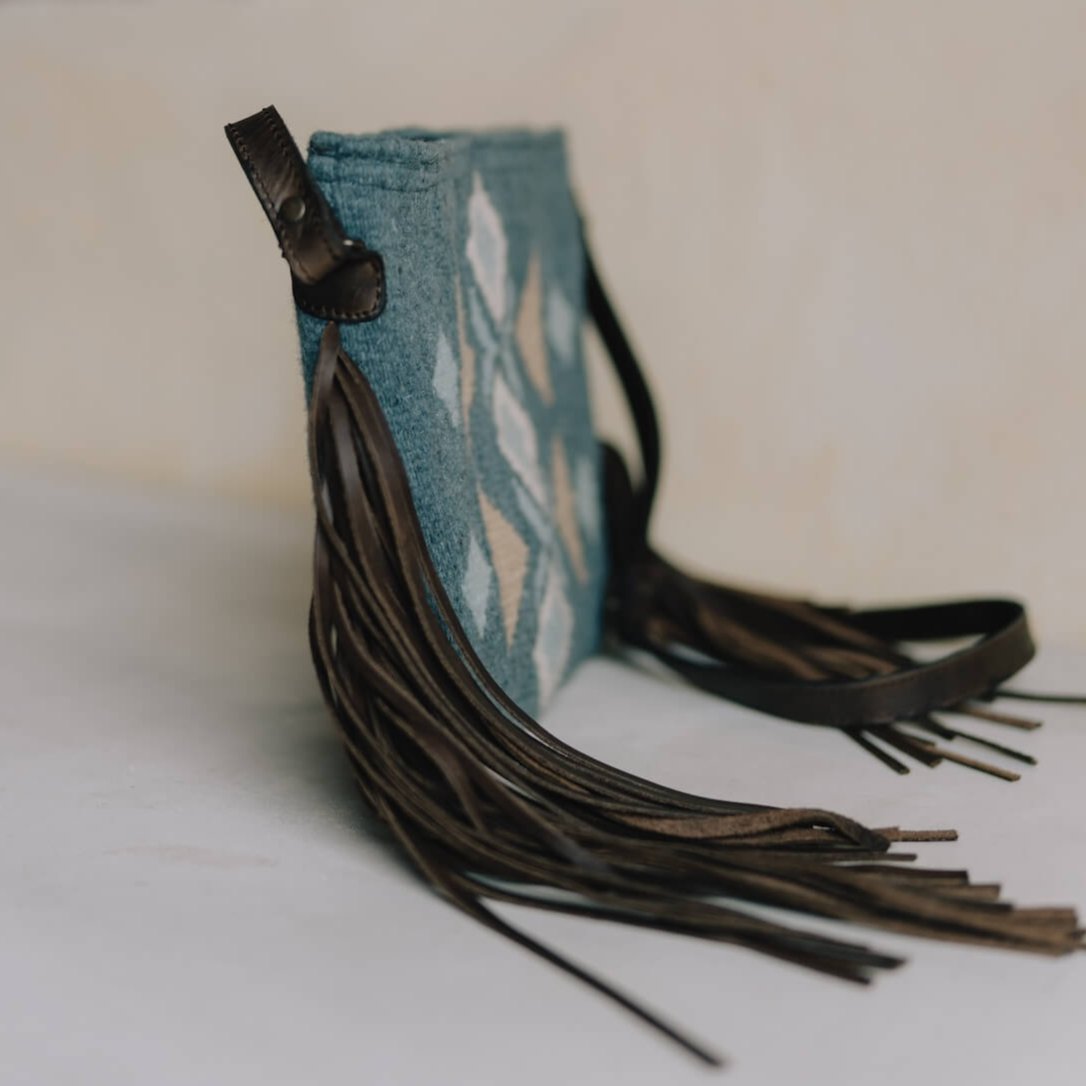 Side view of Festive AMASOUK Jalisco Fringe Crossbody featuring a dark brown leather strap, side fringe, and handwoven wool in blue, heather gray, and honey. Embellished with traditional Zapotec patterns.