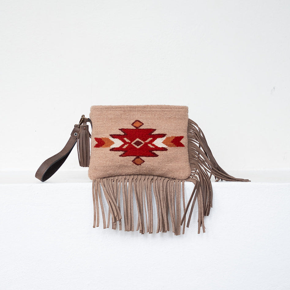 A beige fringed clutch bag with a Southwestern geometric pattern in red, brown, and white on the front flap, shown against a plain white background.