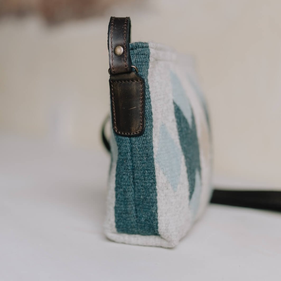 Side view of AMASOUK Espejos Crossbody bag with dark brown leather strap, handwoven wool in blue, heather gray, and ivory, adorned with intricate Zapotec patterns. Stylish and crafted by artisans.