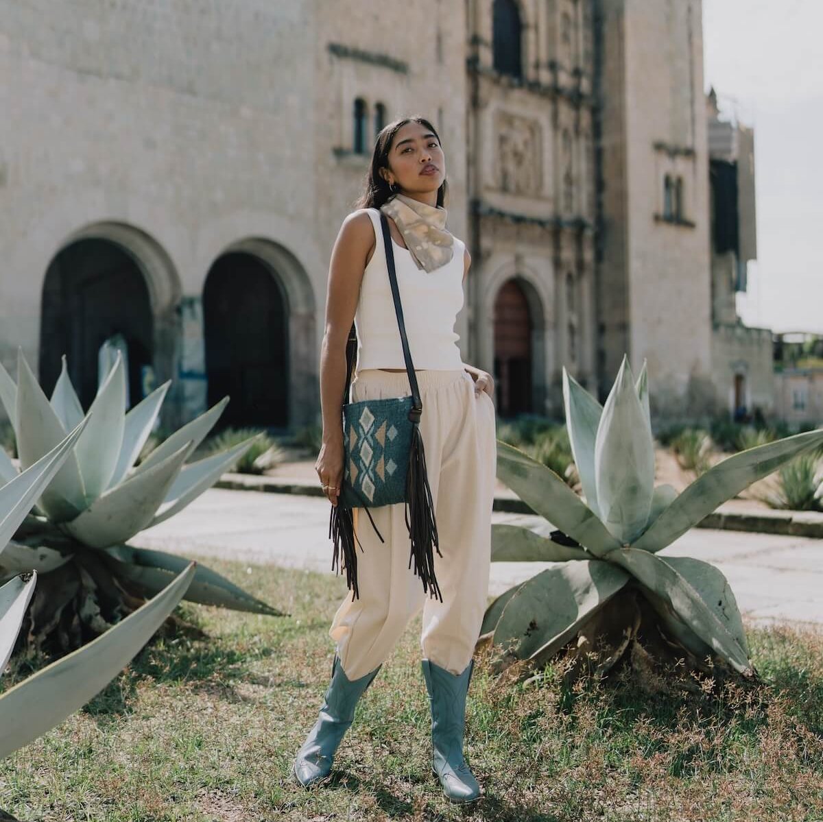 Fashionable woman with an AMASOUK Jalisco Fringe Crossbody bag, showcasing dark brown leather strap, side fringe, and handwoven wool in blue, heather gray, and honey. Embellished with Zapotec patterns.