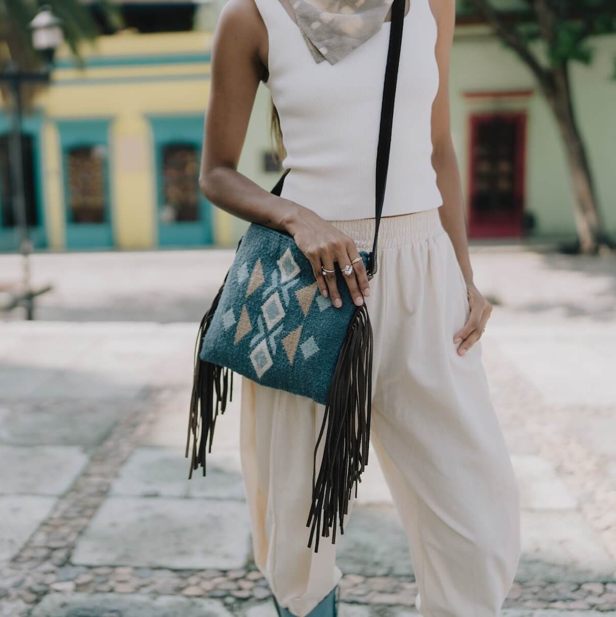 Woman wearing an AMASOUK Jalisco Fringe Crossbody with dark brown leather strap and fringe detail, featuring handwoven wool in blue, heather gray, and honey. Festive and stylish with Zapotec patterns.