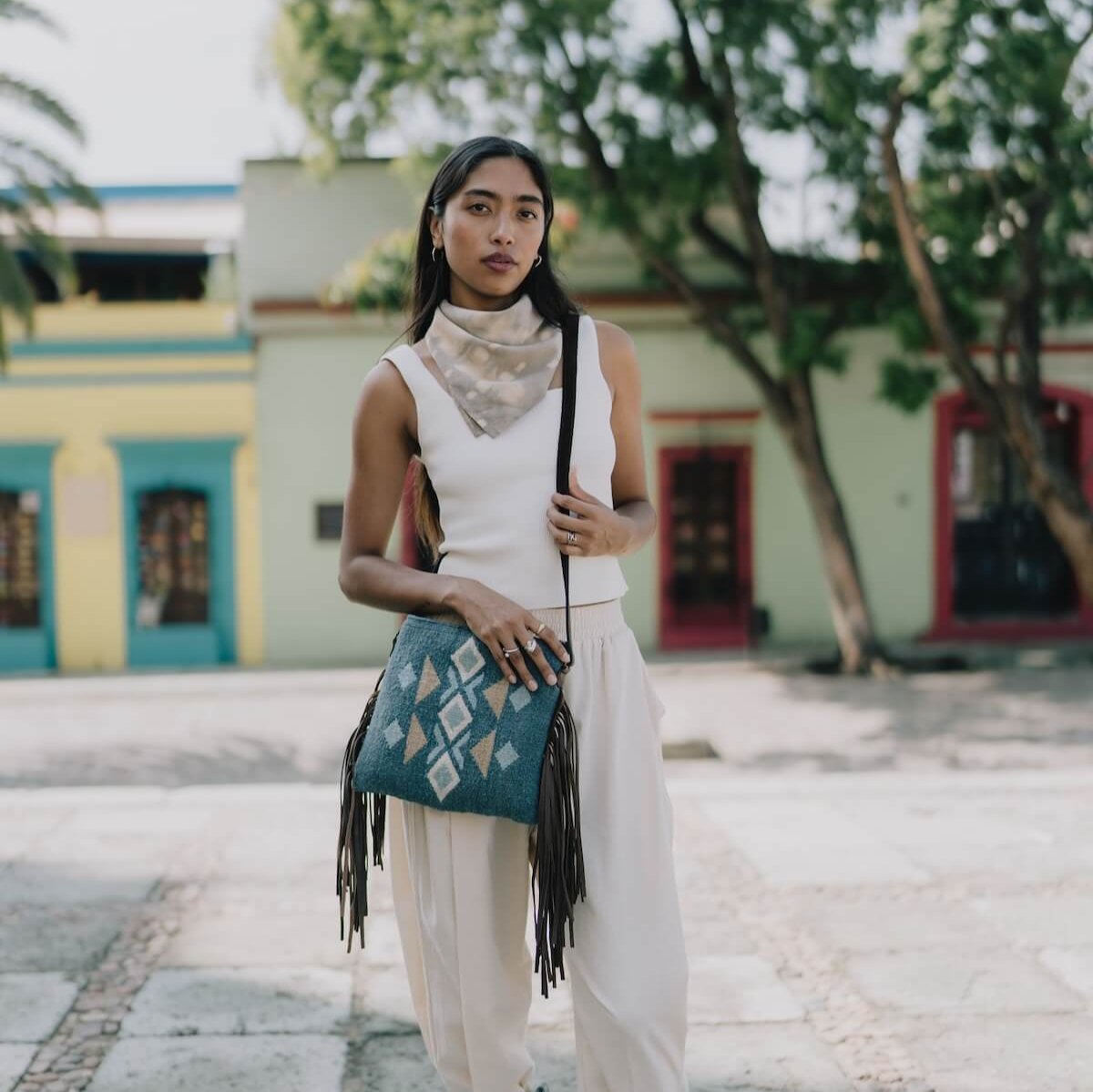 Woman wearing an AMASOUK Jalisco Fringe Crossbody with dark brown leather strap and fringe detail, featuring handwoven wool in blue, heather gray, and honey. Festive and stylish with Zapotec patterns.