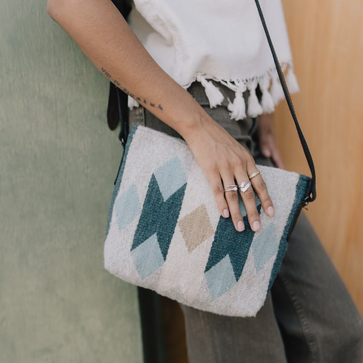 Woman wearing an AMASOUK Espejos Crossbody bag, handwoven from wool in blue, heather gray, and ivory with a dark brown leather strap. Featuring Zapotec patterns, handcrafted by skilled artisans.