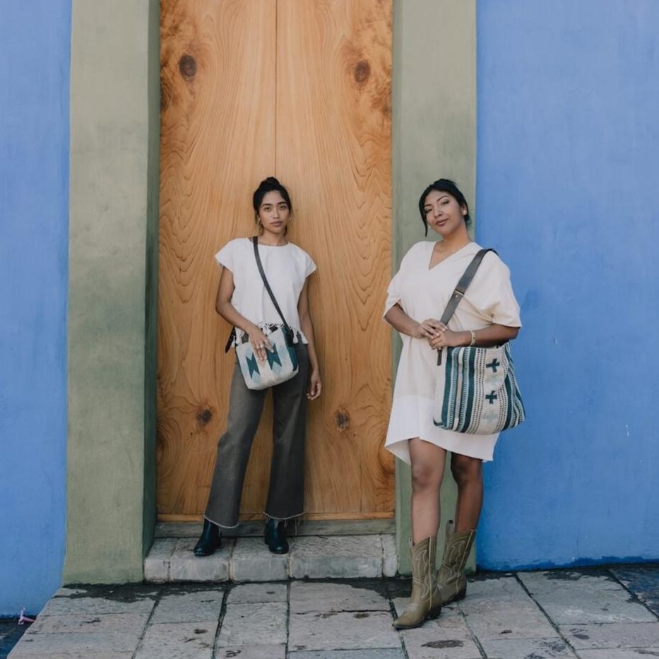 Chic woman carrying an AMASOUK Espejos Crossbody bag with a dark brown leather strap, blue, heather gray, and ivory wool, detailed with Zapotec patterns. Perfect for day-to-night transitions.