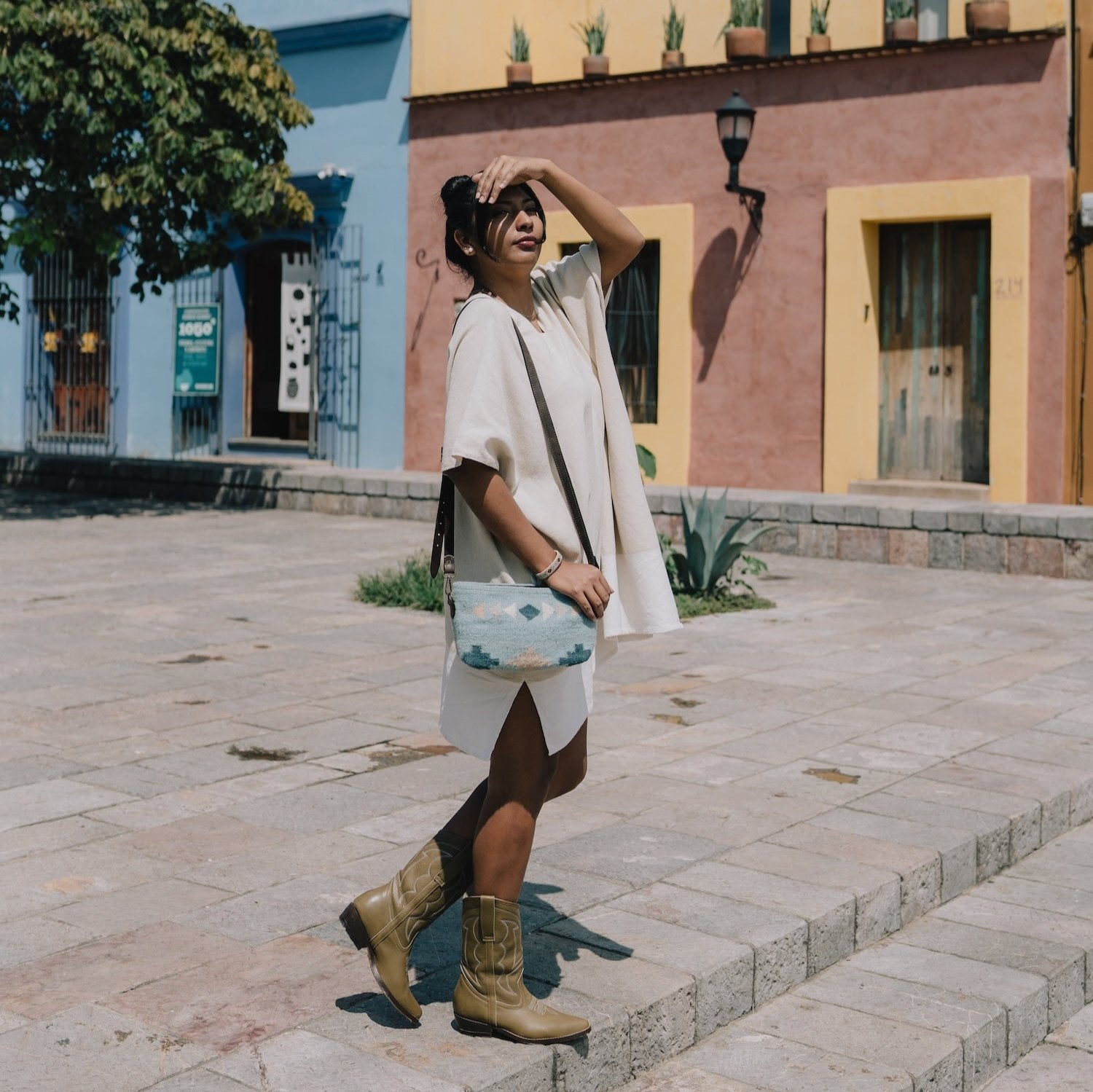 Fashionable woman holding the AMASOUK Cielito Convertible Clutch/Wristlet/Crossbody Bag, featuring a handwoven wool design with a Zapotec pattern in blue tones. A versatile 3-in-1 accessory.