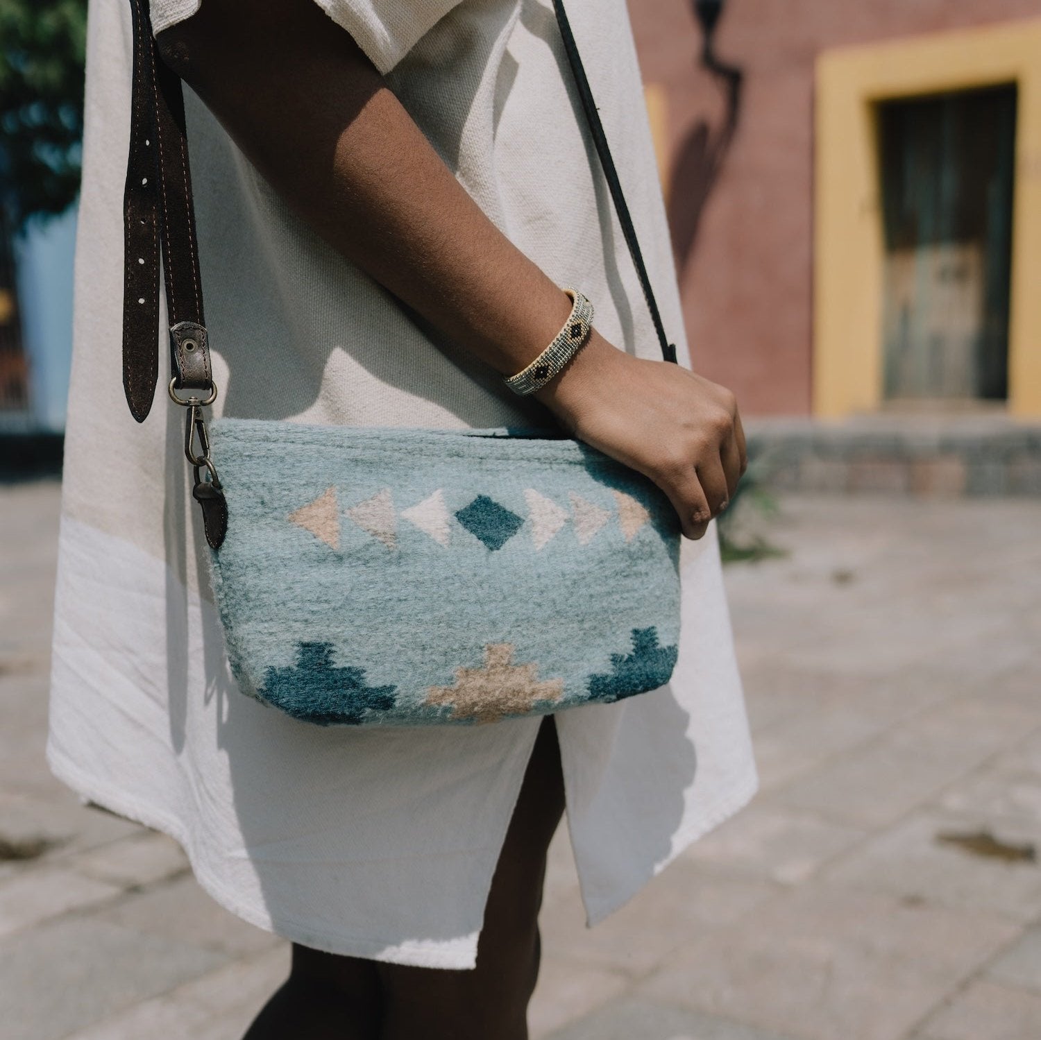 Effortlessly stylish woman carrying the Cielito Convertible Bag by AMASOUK, featuring a Zapotec pattern in handwoven wool and elegant blue hues. A versatile 3-in-1 design.