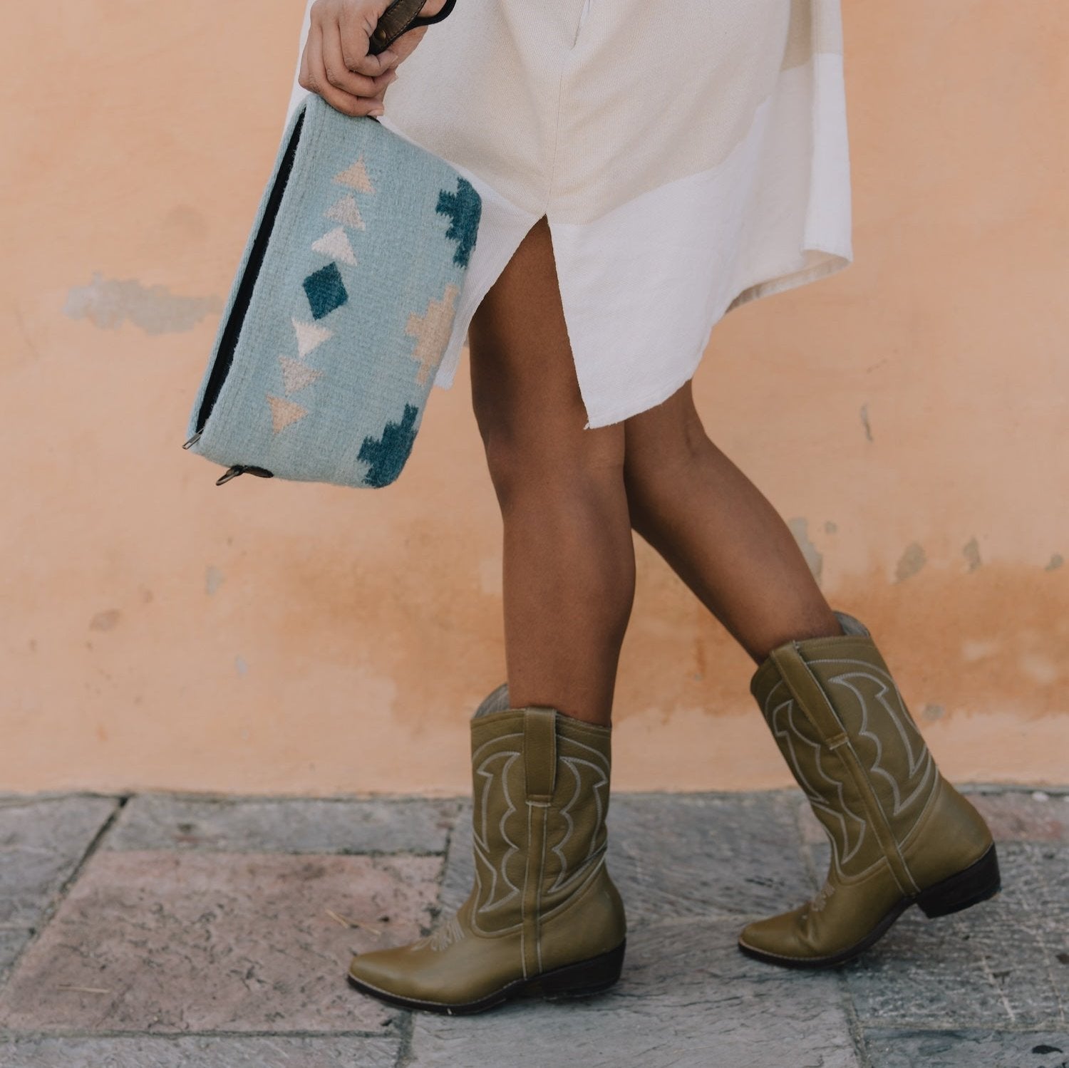 Fashionable woman holding the AMASOUK Cielito Convertible Clutch/Wristlet/Crossbody Bag, featuring a handwoven wool design with a Zapotec pattern in blue tones. A versatile 3-in-1 accessory.