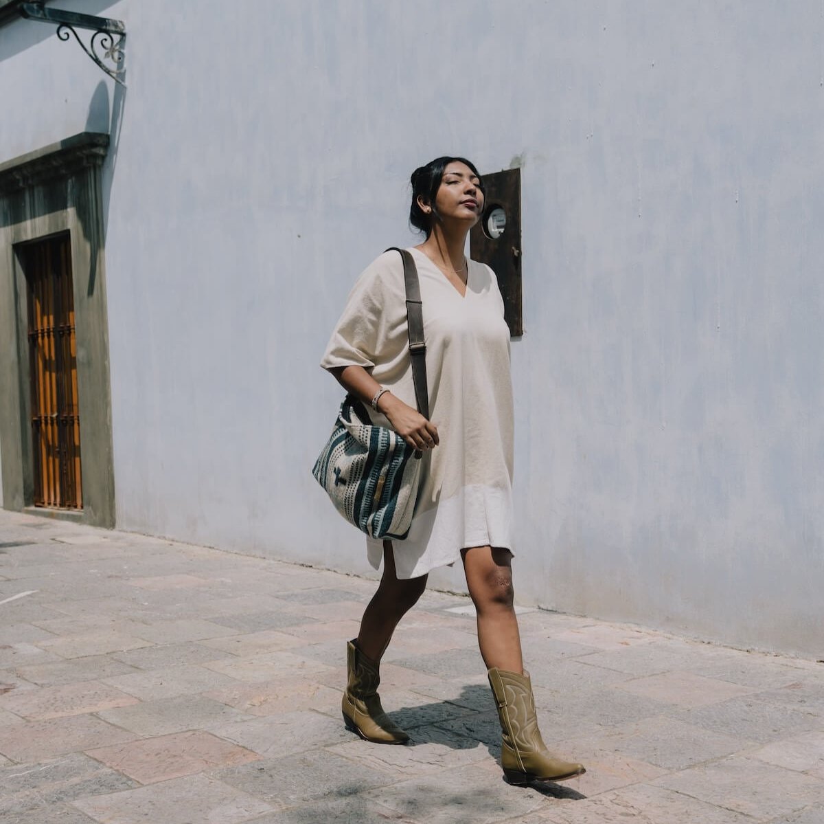 Woman holding an AMASOUK Copalita handwoven wool and leather convertible shoulder/crossbody bag in blue, cream, honey, and gray. Ideal for carrying essentials throughout the day.