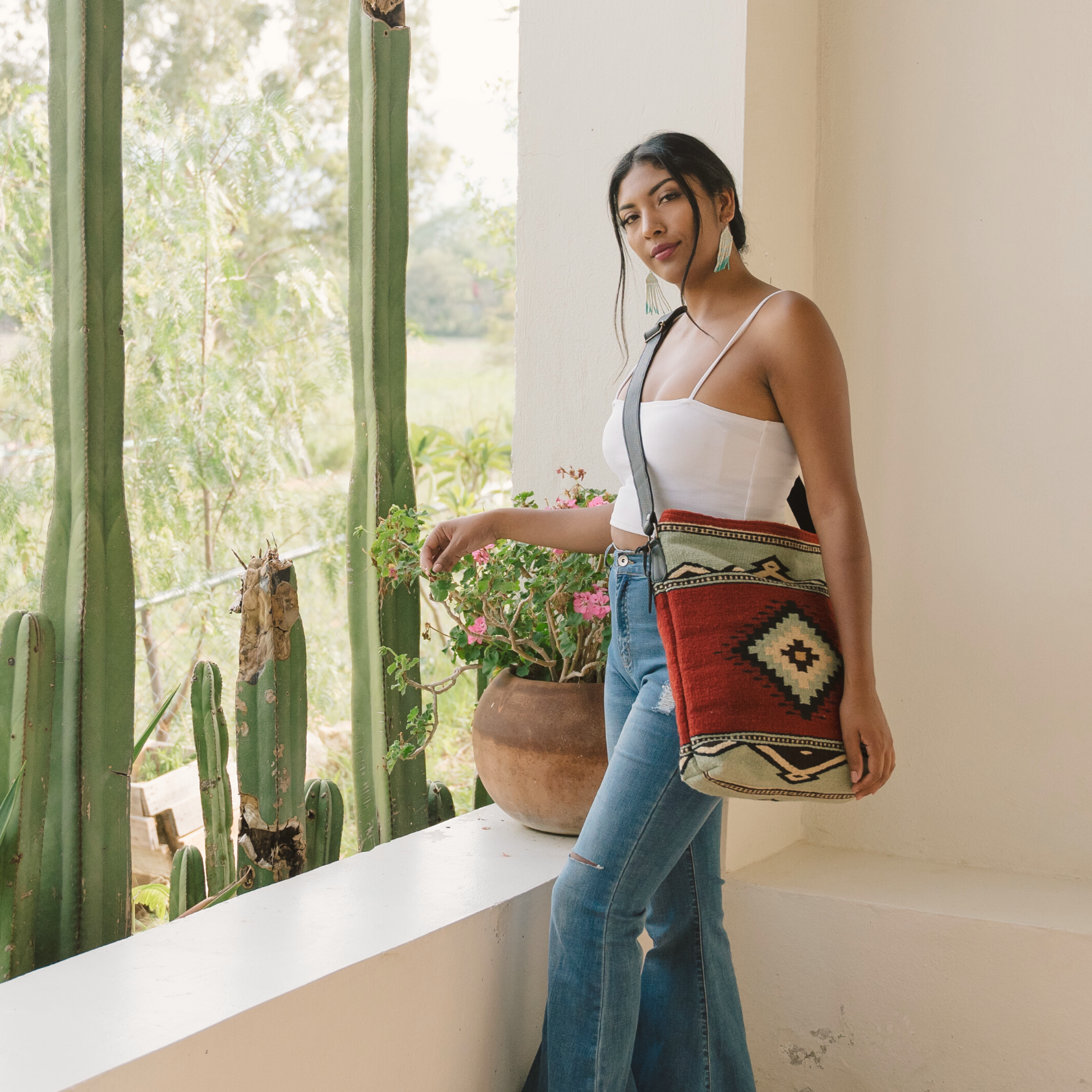 Woman carrying an AMASOUK handwoven wool convertible shoulder/crossbody bag with Adobe + Azul name, featuring a Zapotec pattern in adobe red and mint green. Perfect for errands, work, or casual outings.